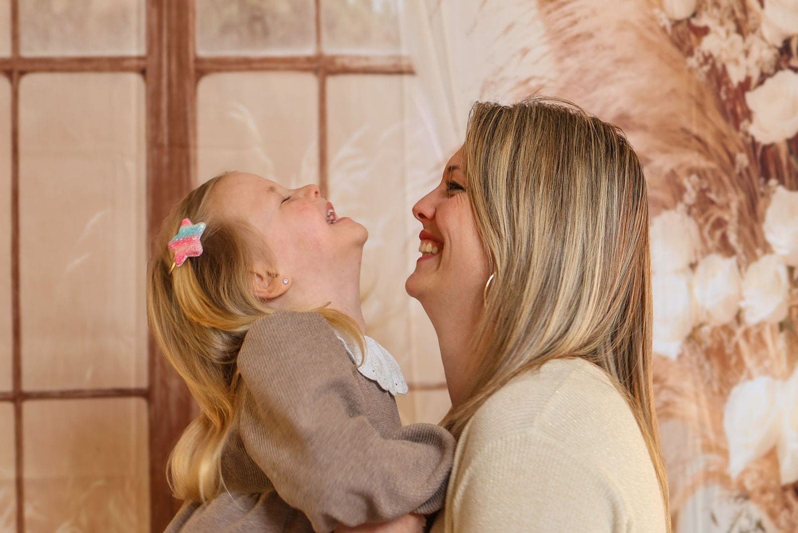 Une petite fille et sa maman éclatent de rire, front contre front, au studio.