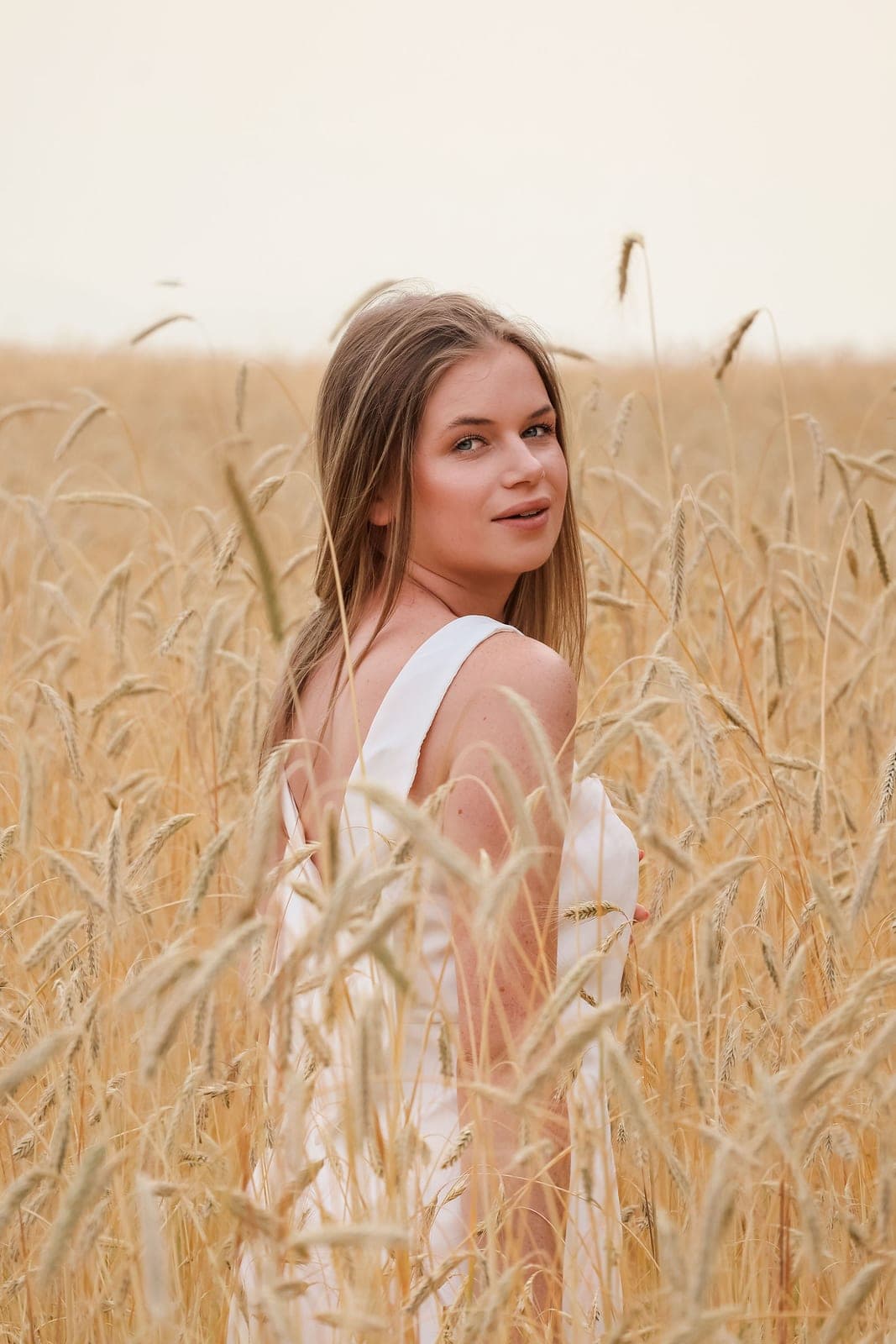 Une jeune femme en robe blanche se retourne dans un champ de blé.