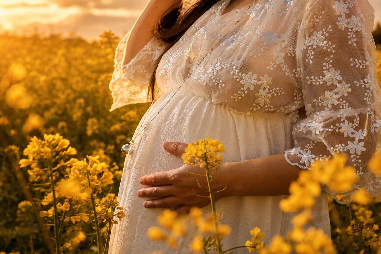 Les mains d’une future maman posées sur son ventre, un bouquet de fleurs jaunes à la main, dans un champ doré.