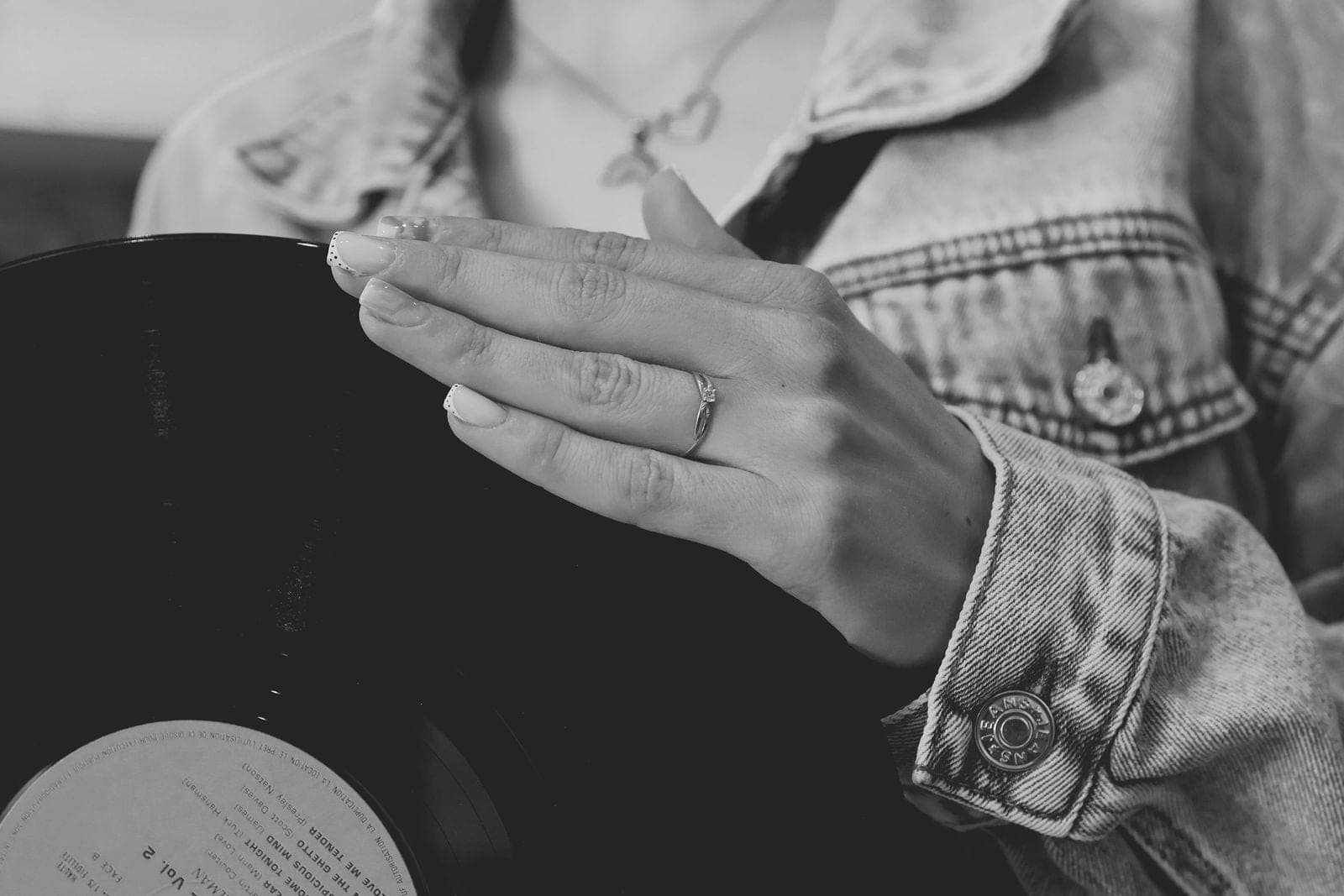 En noir et blanc, la main posée sur la veste en jean, bague au doigt.
