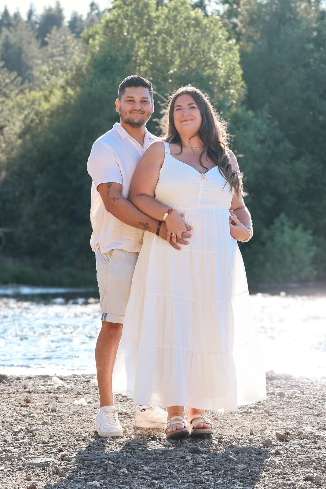 Les futurs mariés enlacés au bord du lac, en tenues claires.