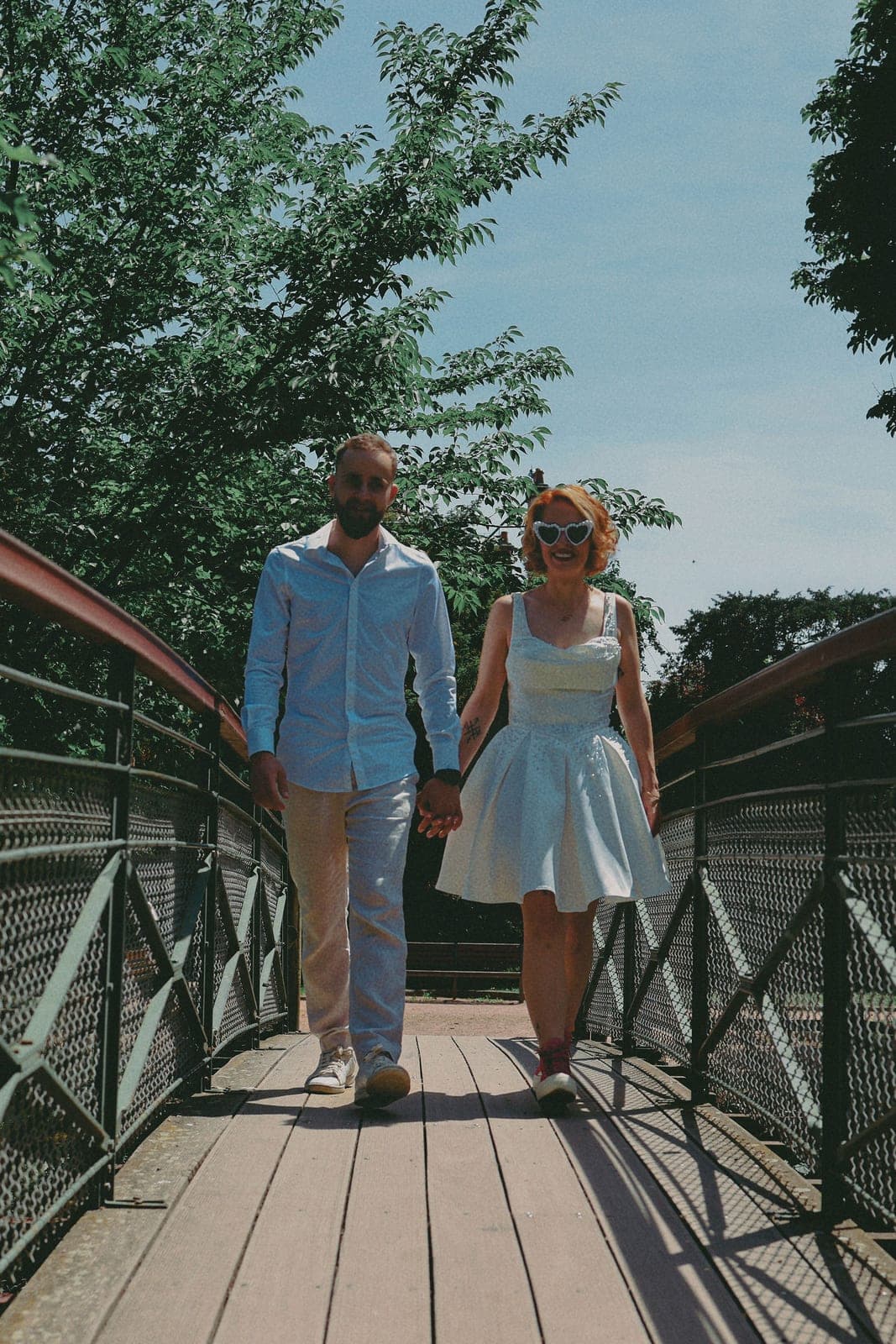 Main dans la main sur la passerelle rouge, lunettes en cœur.