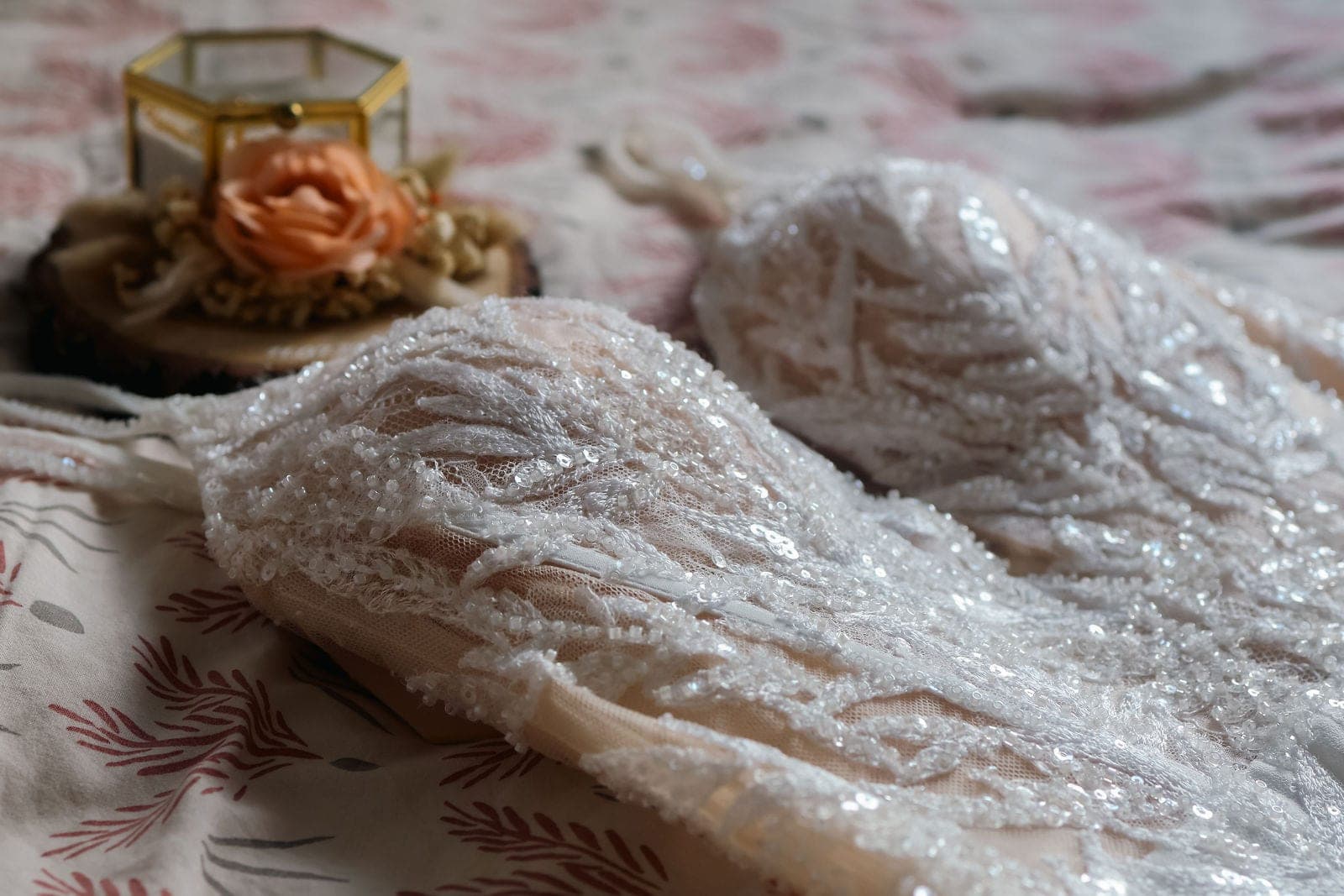 La robe en dentelle perlée posée sur le lit, à côté des alliances.