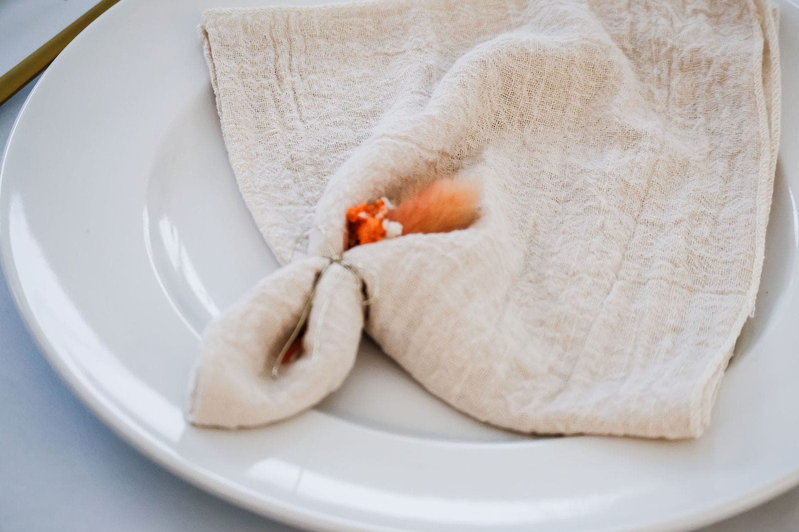 La serviette pliée sur l’assiette, nouée d’une fleur orange.