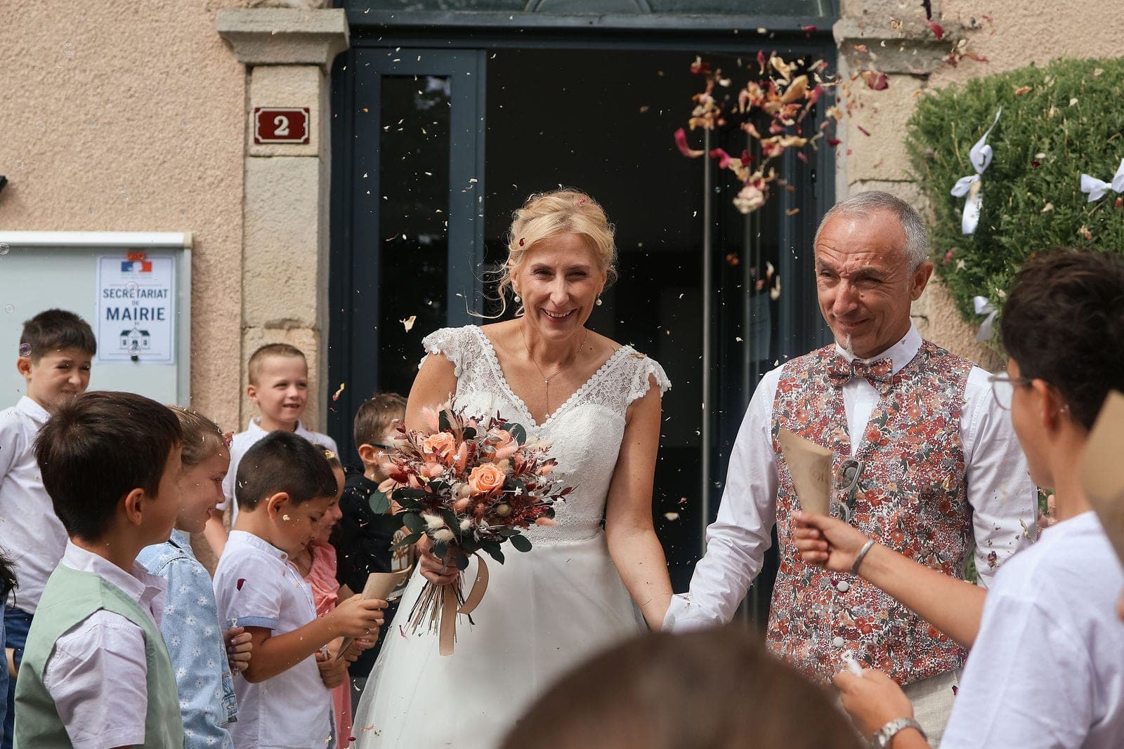 La sortie sous une pluie de pétales, la mariée serre son bouquet.