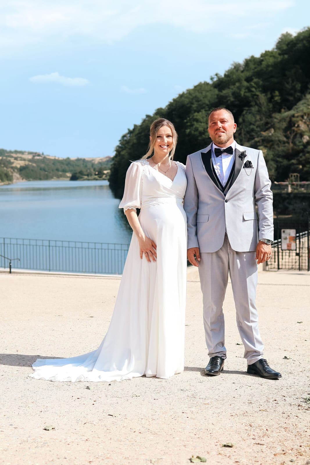 Le couple pose au bord du lac, robe fluide et costume gris perle.