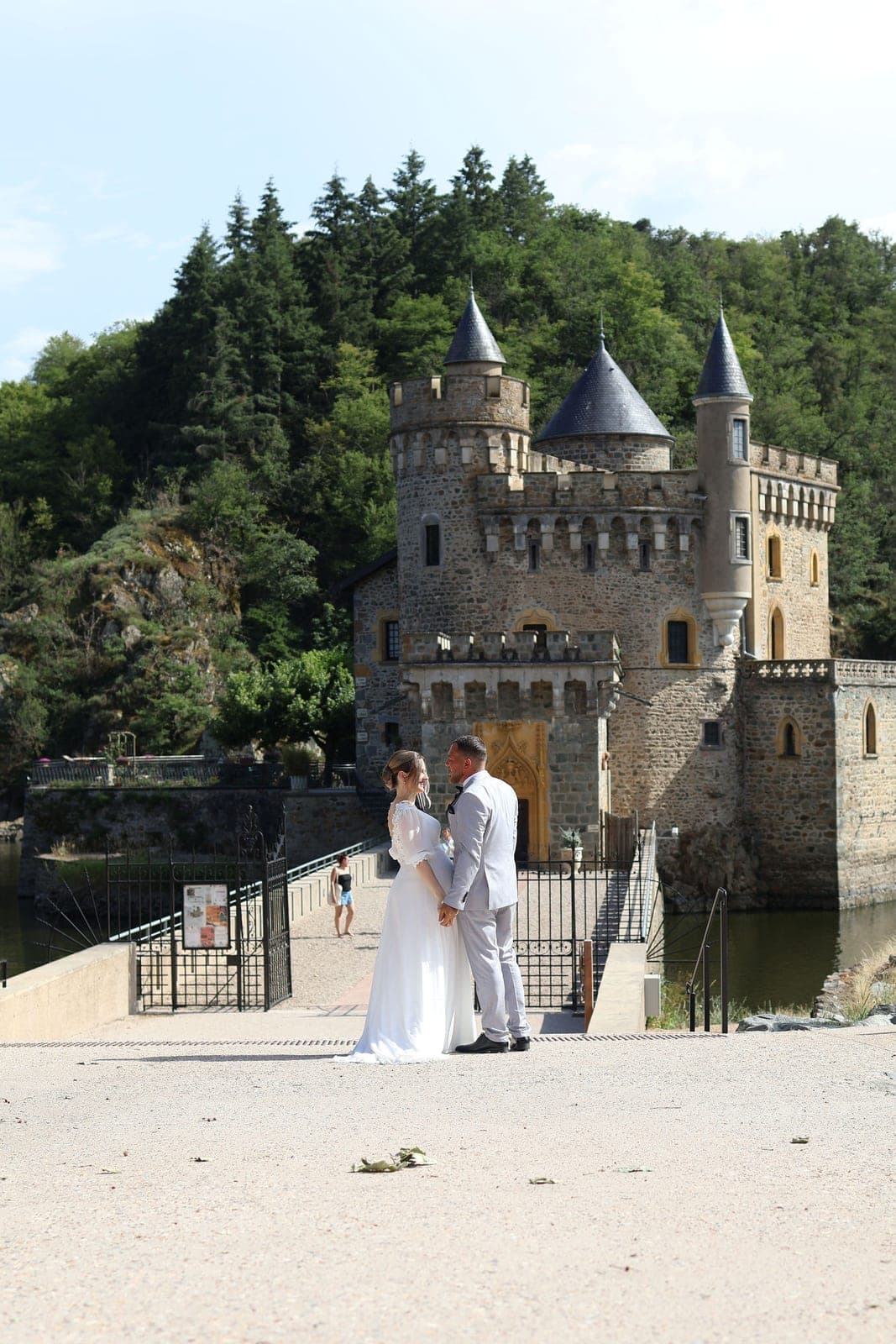 Les mariés minuscules devant le château, entre les tours et la rivière.