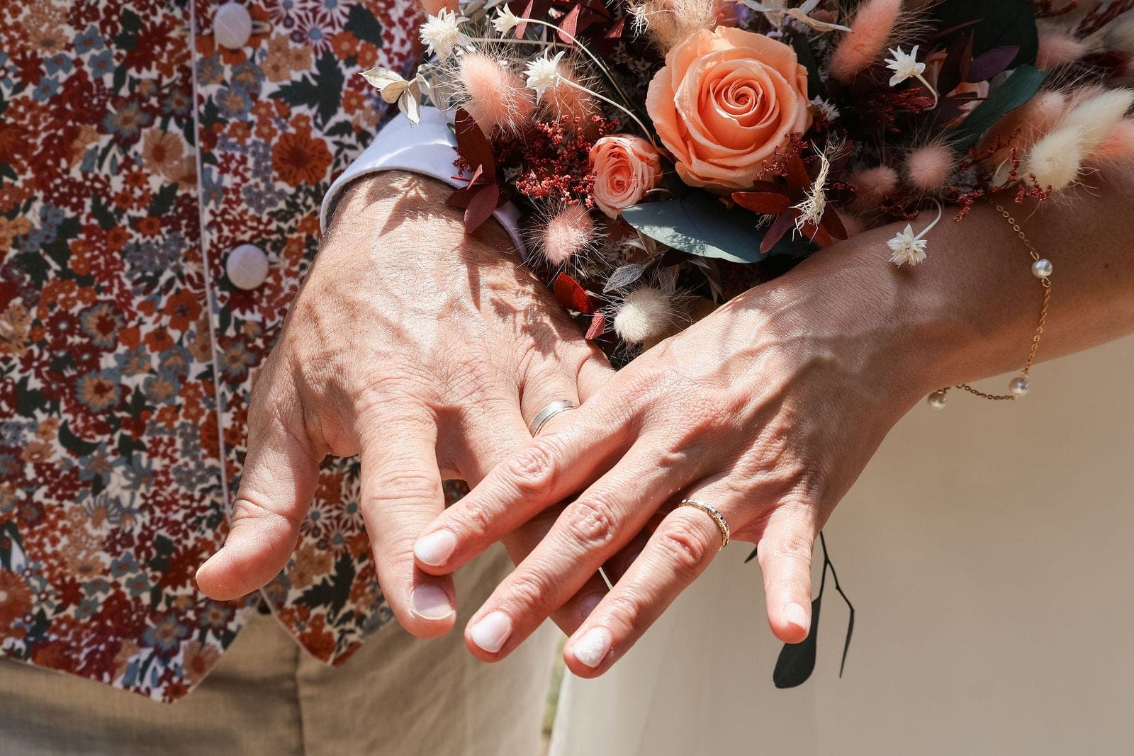 Les mains des mariés réunies au-dessus du bouquet de fleurs séchées.