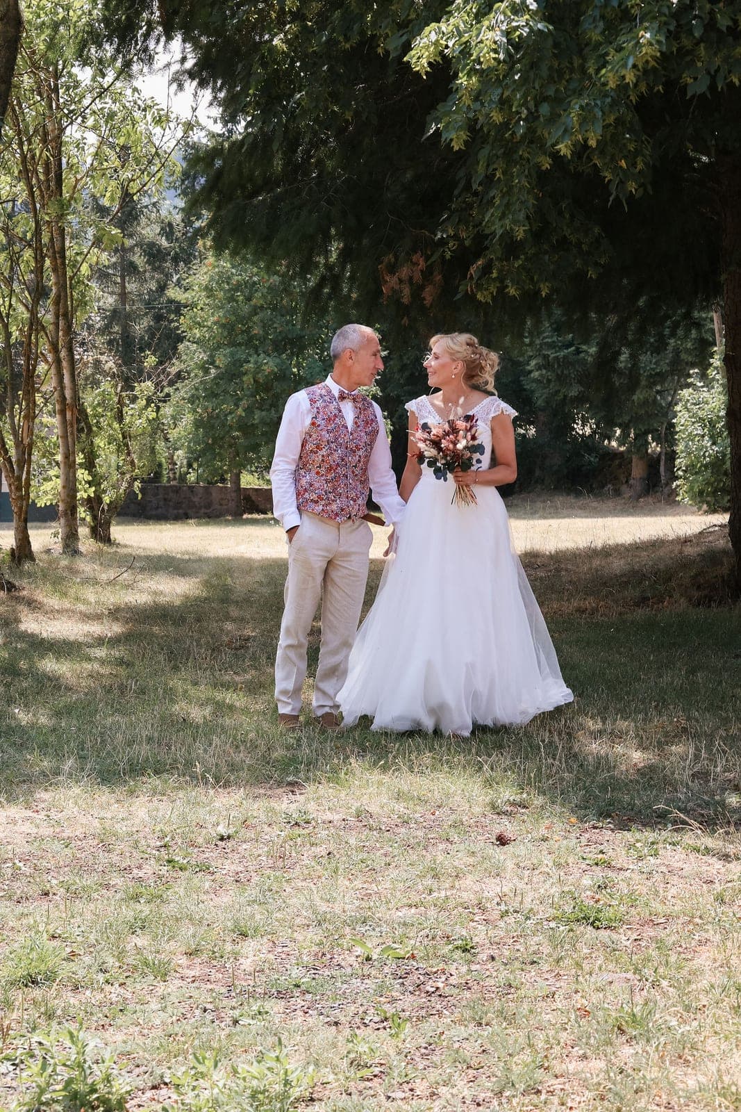 Les mariés marchent dans le sous-bois, le bouquet à la main.