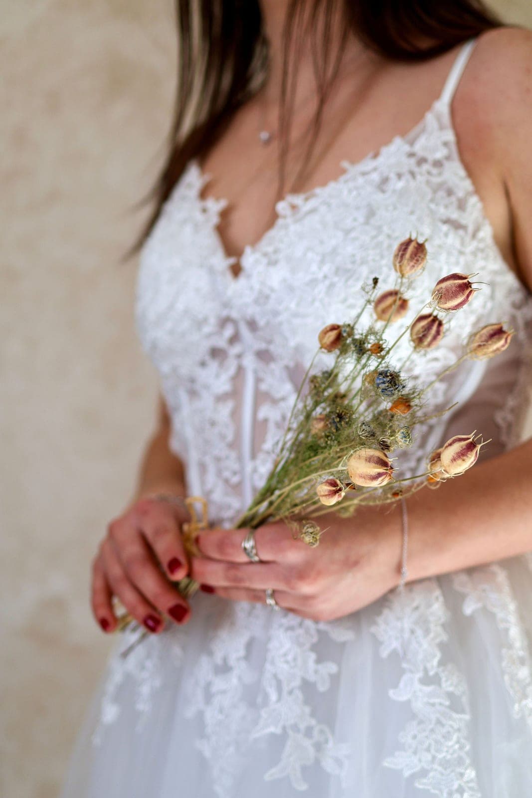 La mariée tient son bouquet de fleurs séchées contre sa robe.