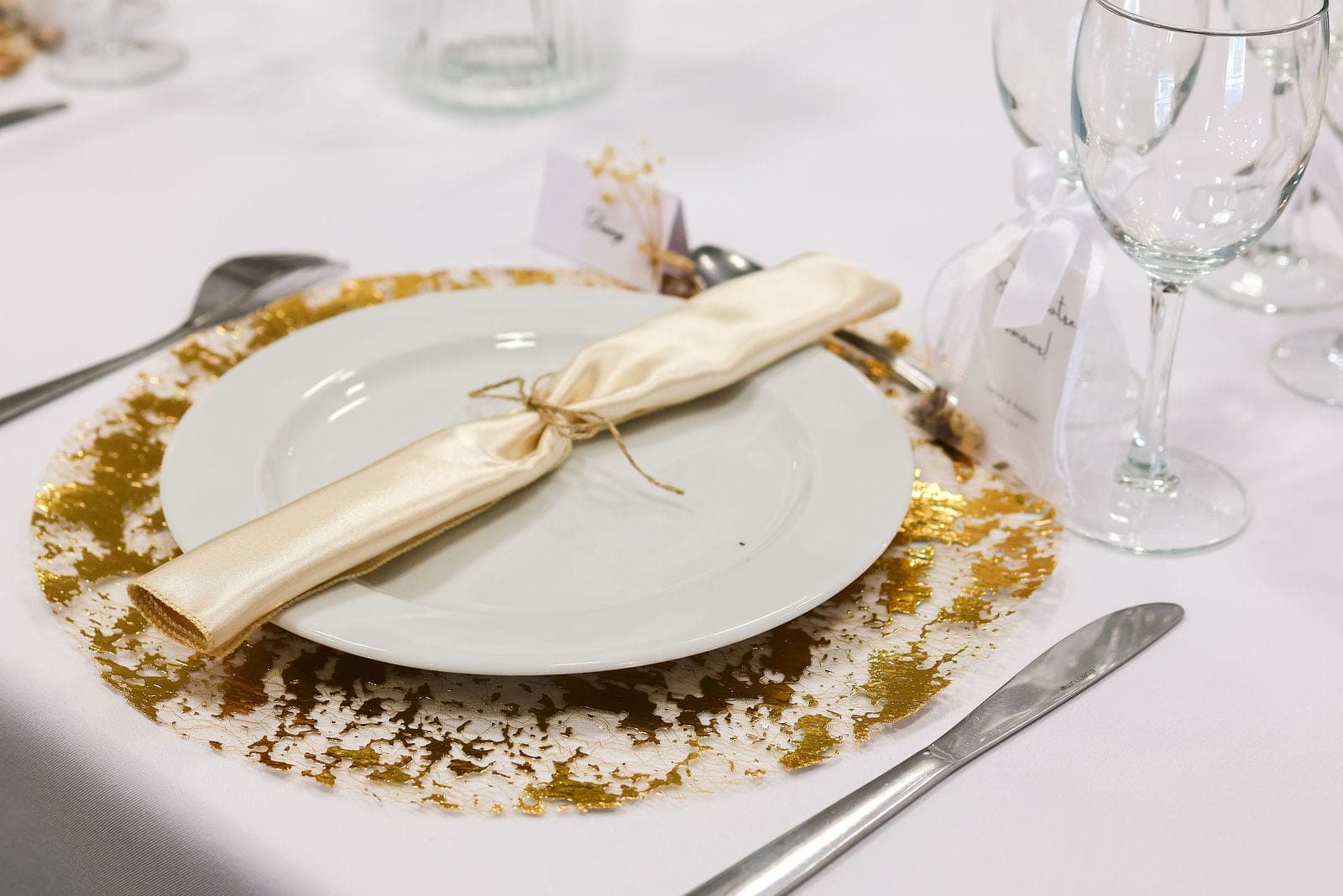 L’assiette de présentation dorée, serviette écrue nouée de raphia.