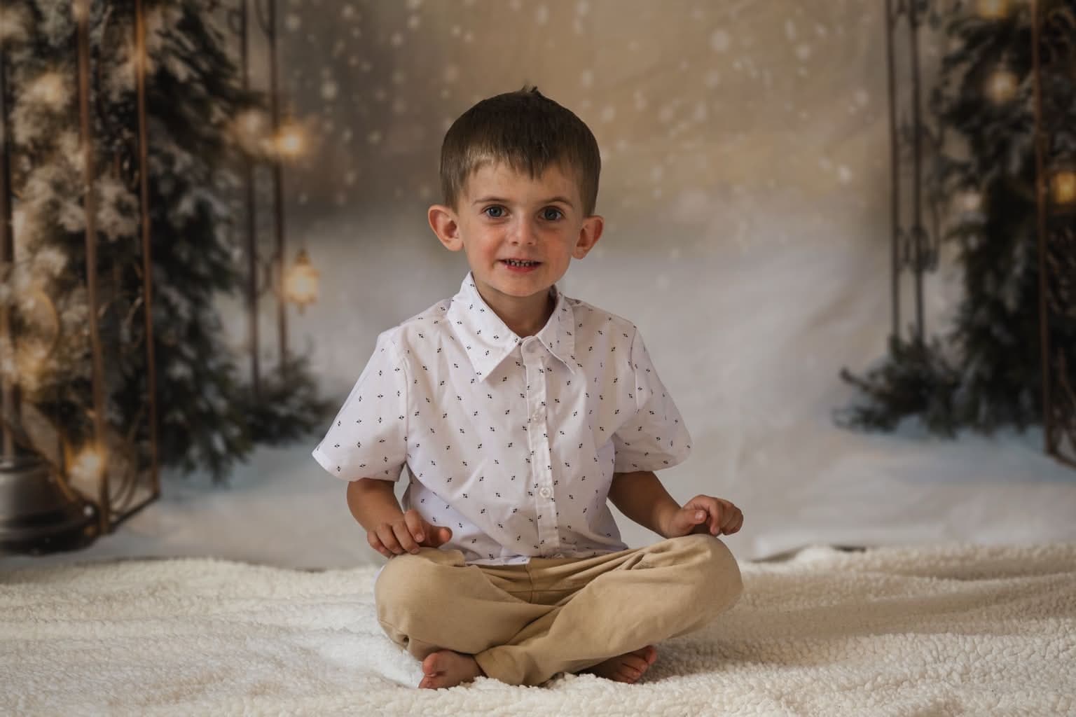 Portrait d’un petit garçon assis en tailleur, décor de Noël aux lumières dorées