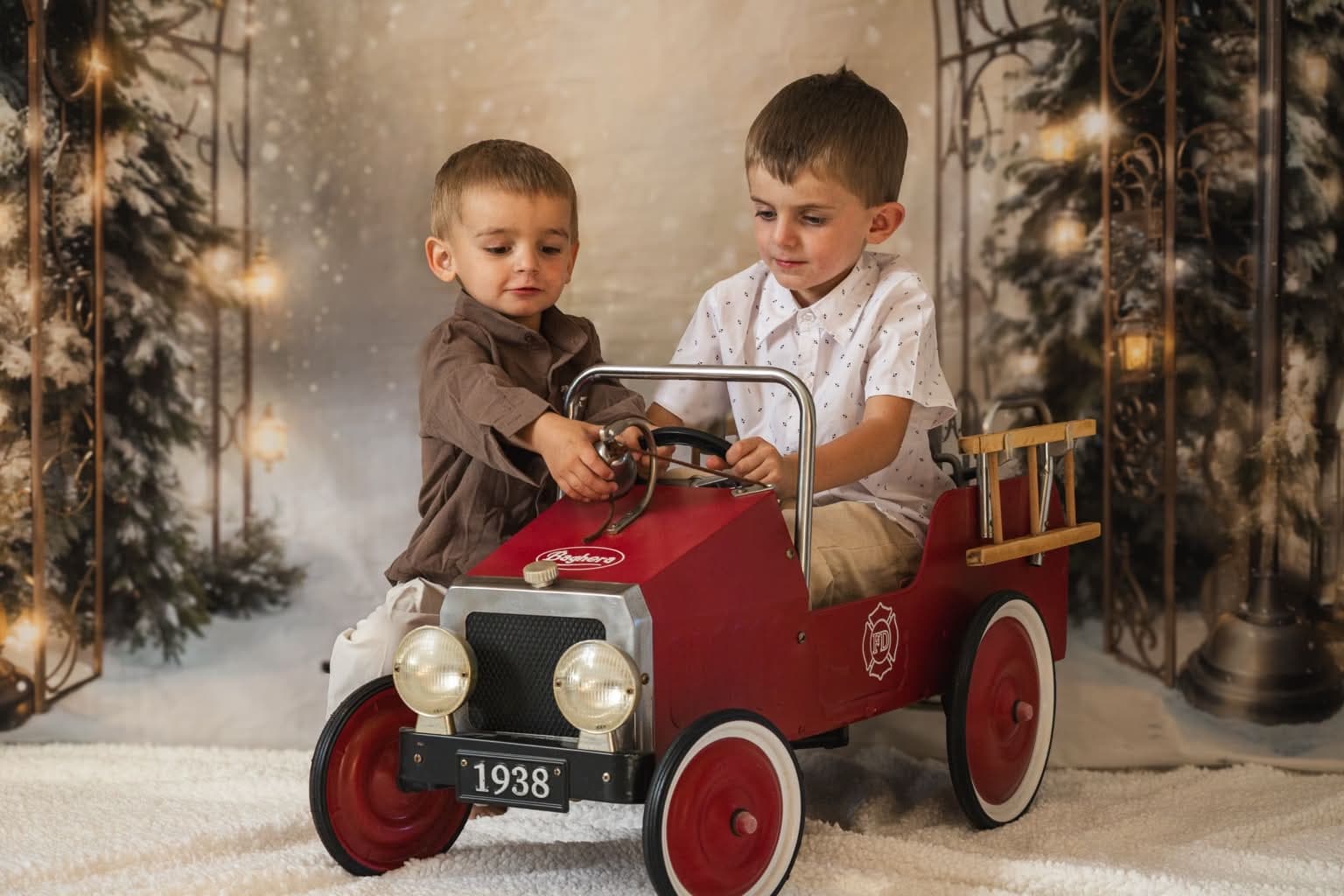 Deux frères jouant ensemble dans une voiture à pédales rouge, décor de Noël