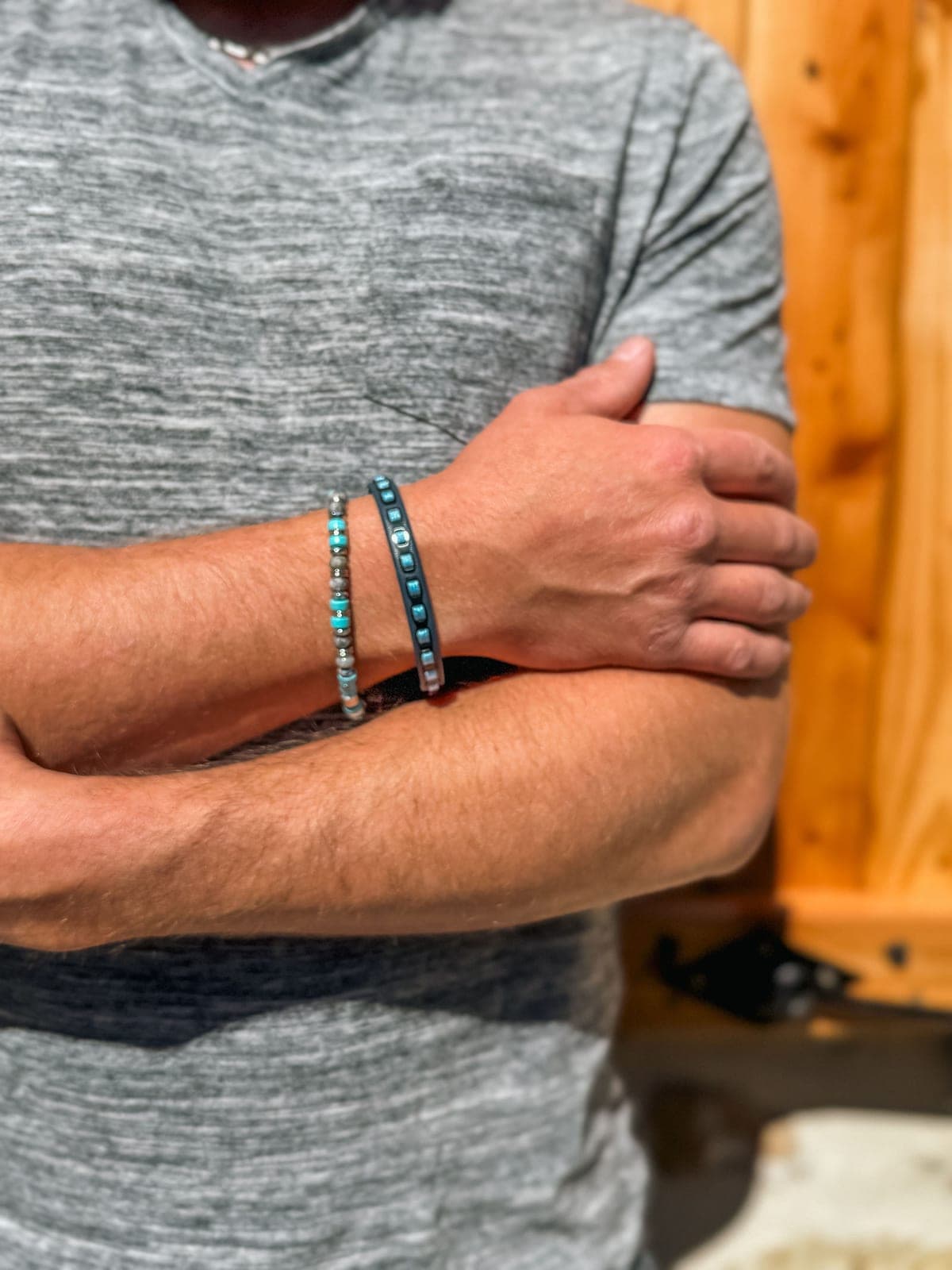 Deux bracelets portés, bras croisés sur un tee-shirt gris.