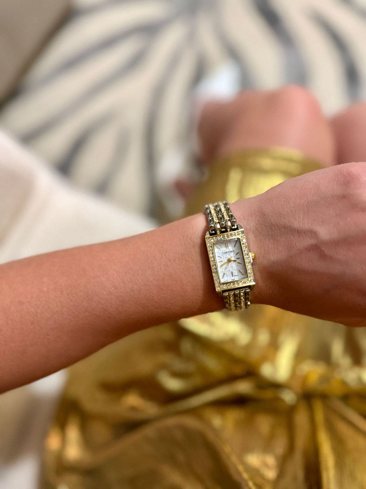 Une montre dorée au poignet, sur un drap clair.