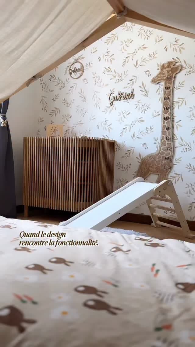 Une chambre d’enfant claire, lit à barreaux et girafe en bois.