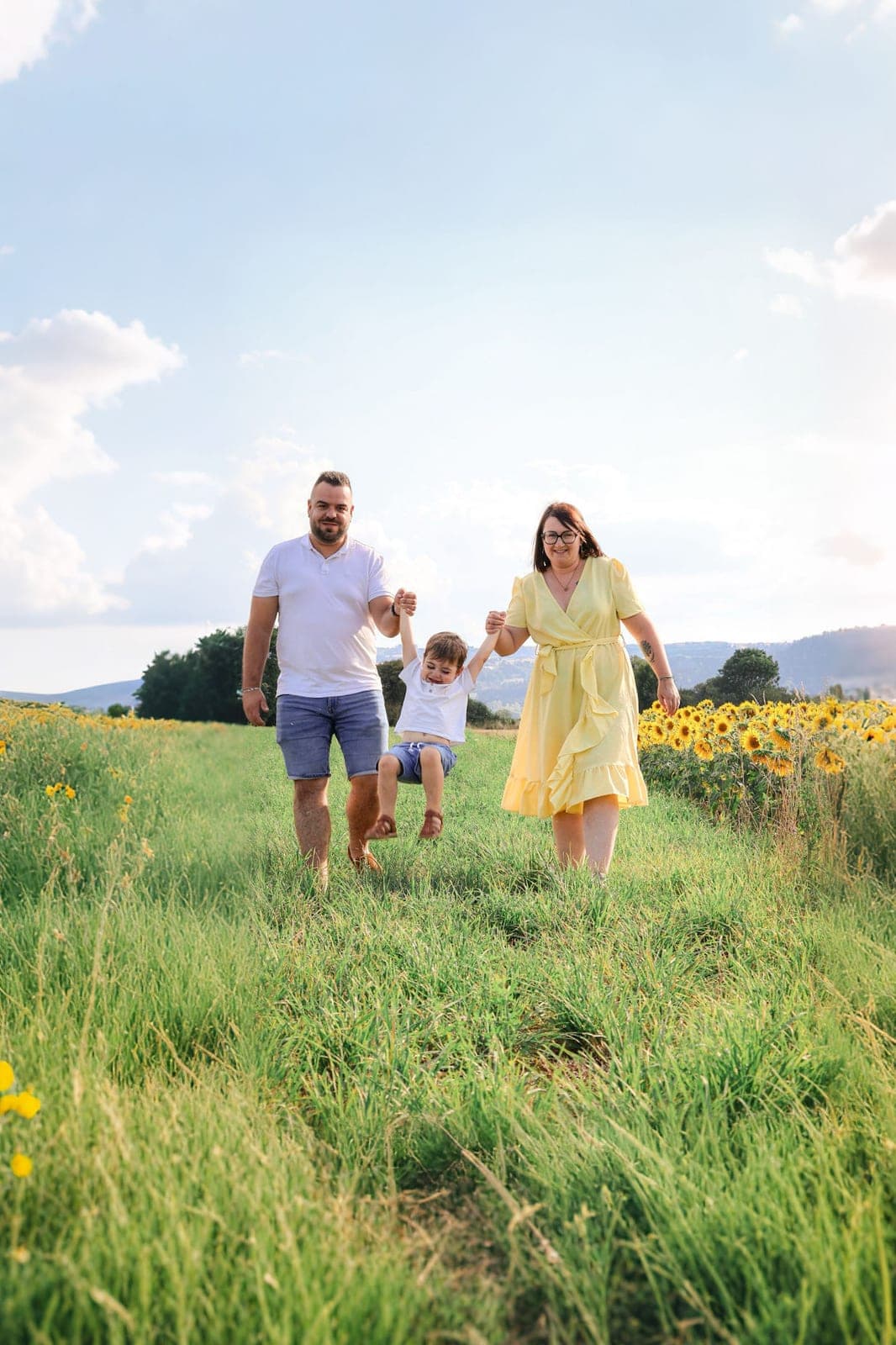 Une famille marche main dans la main dans un pré, la petite portée entre papa et maman.