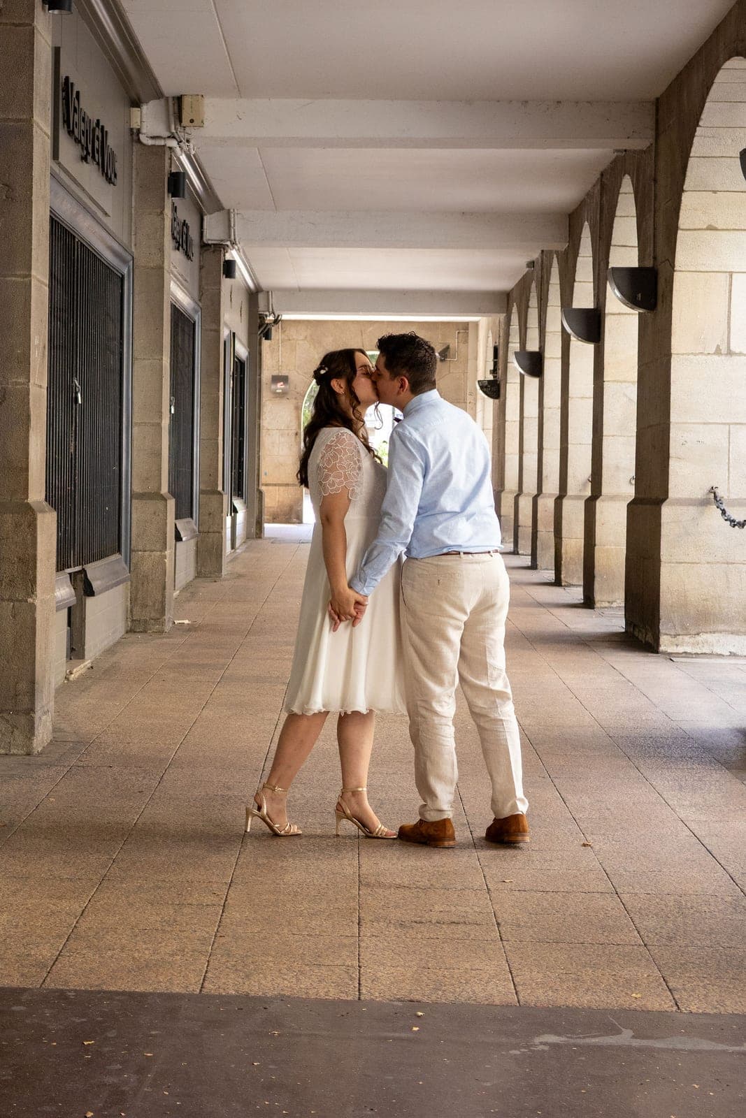 Un baiser sous les arcades, robe claire et lumière d’été.