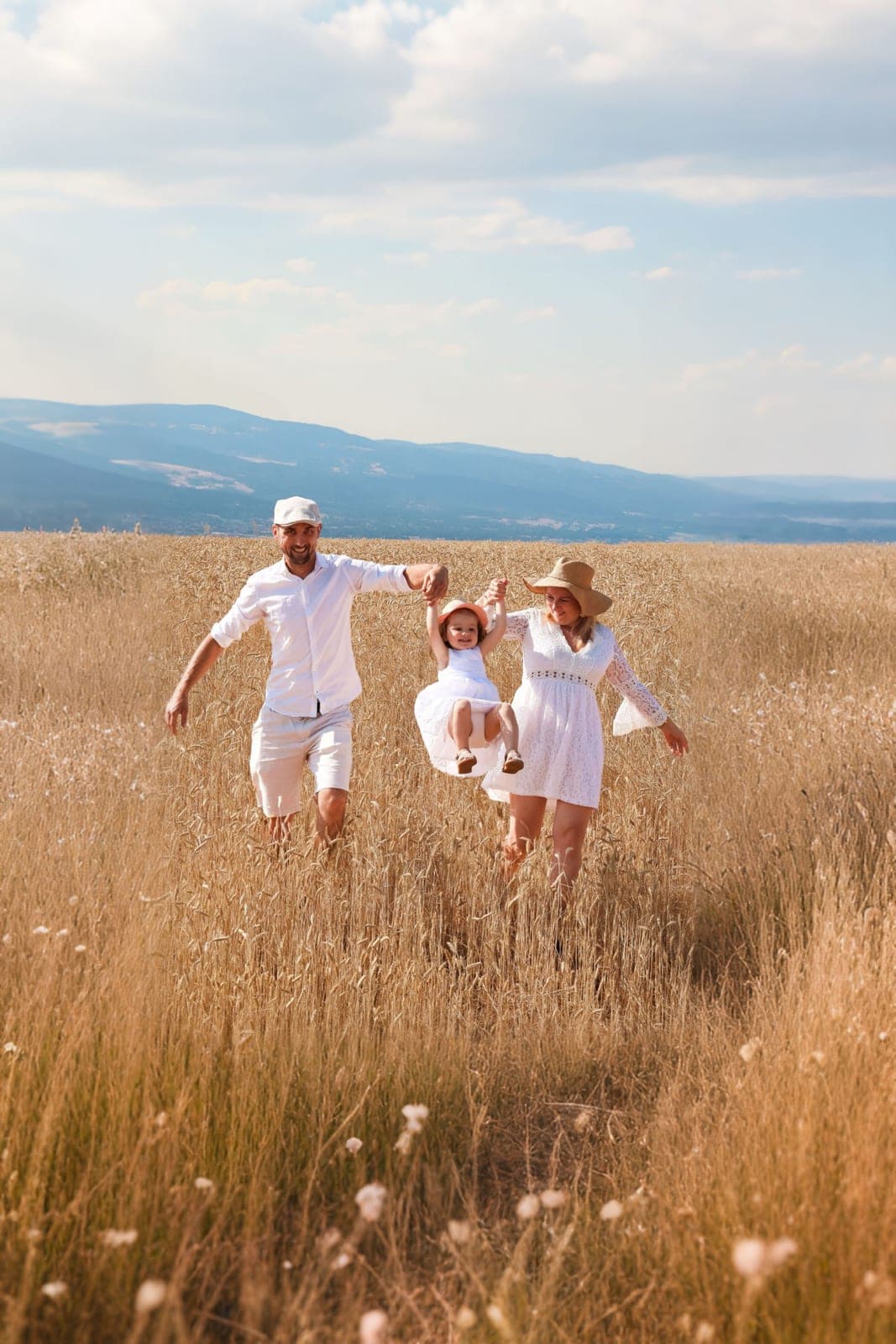 Une famille court dans les blés, la petite fille soulevée par ses parents.