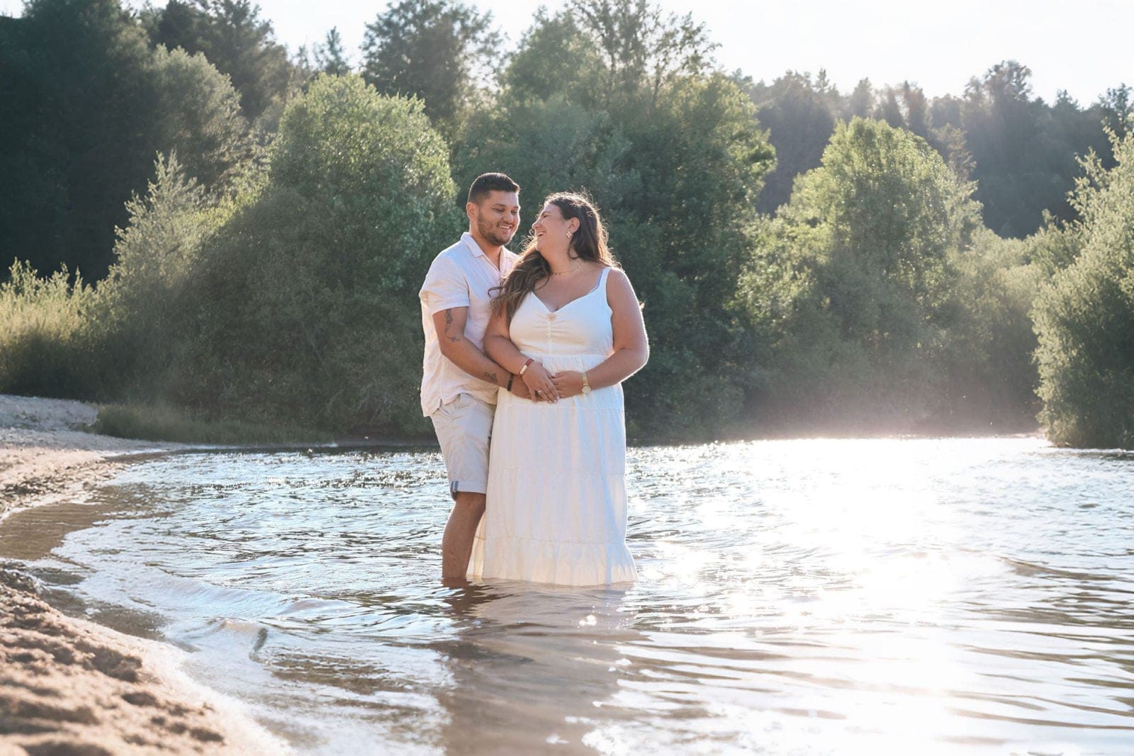 Un couple enlacé, les pieds dans l’eau de la rivière, à contre-jour.
