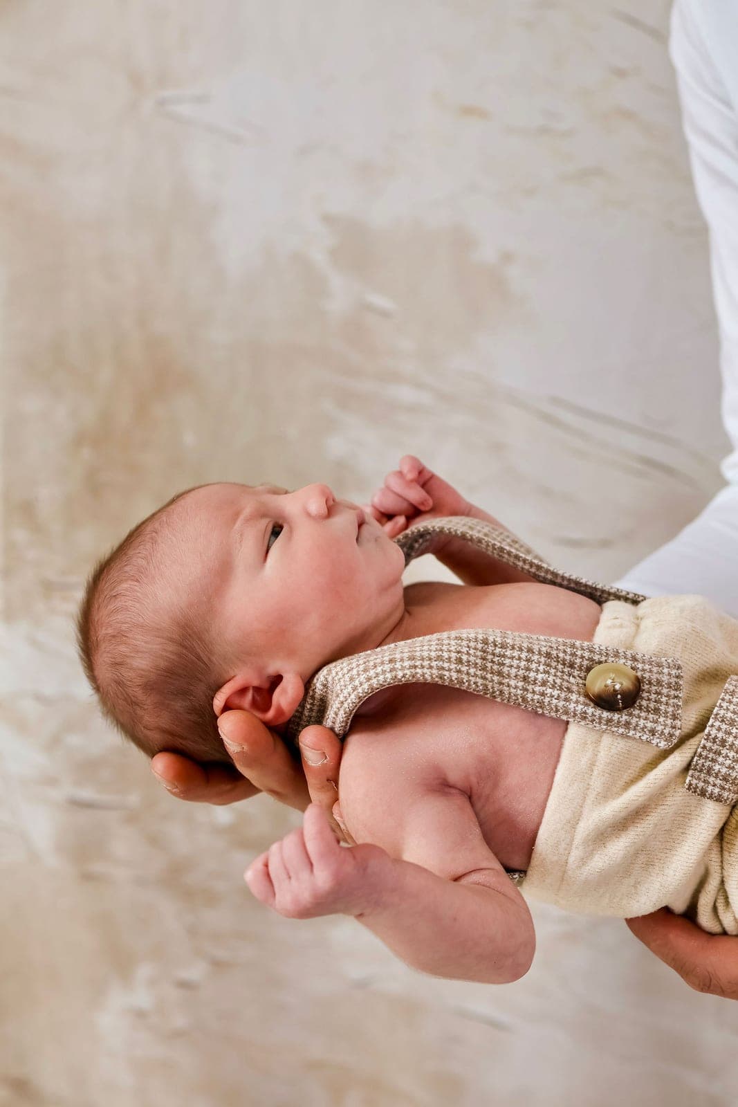 Un nouveau-né en tenue à bretelles, tenu dans les mains de son papa.