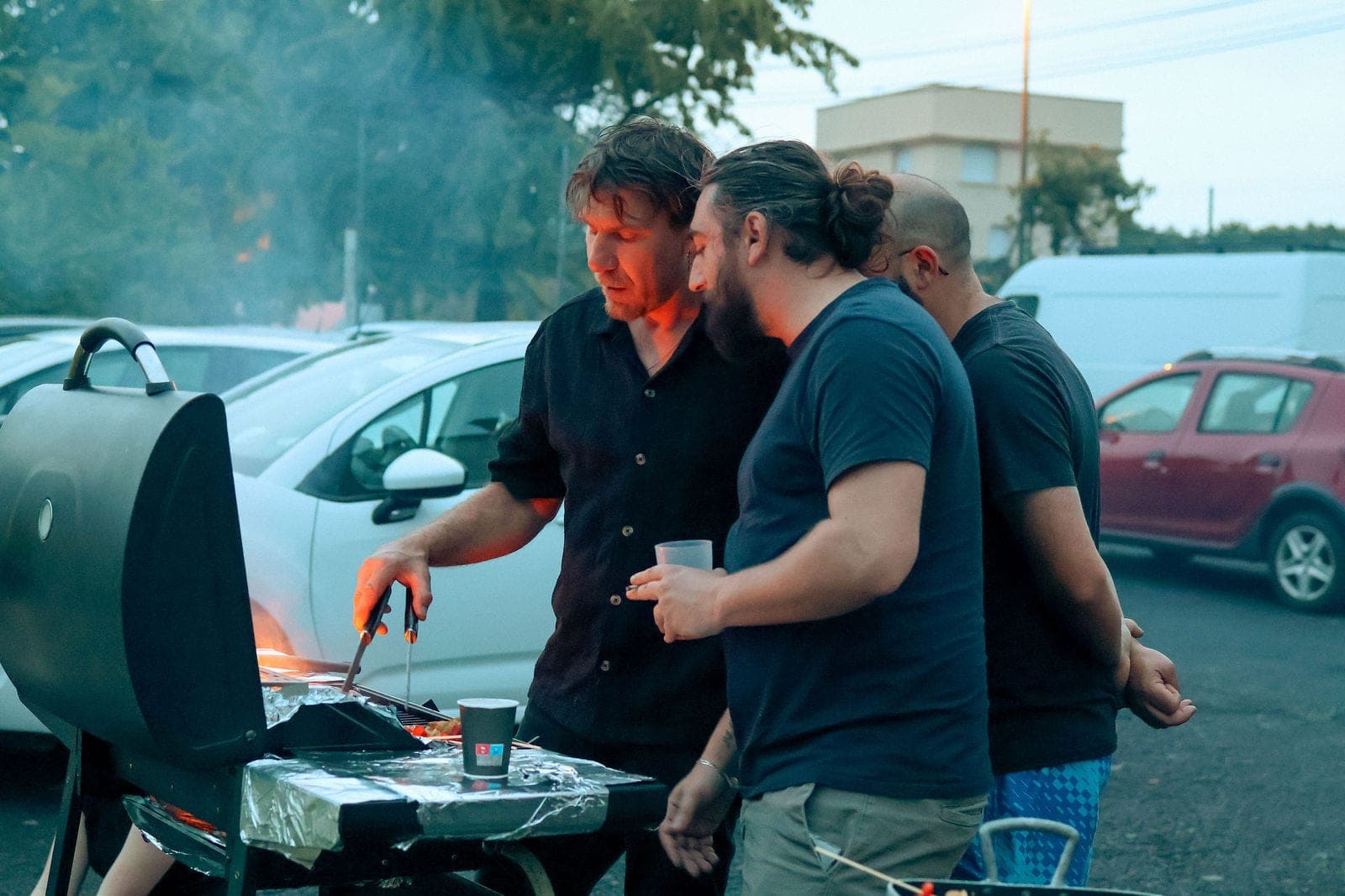 Autour du barbecue, verres à la main, dans la fumée du soir.