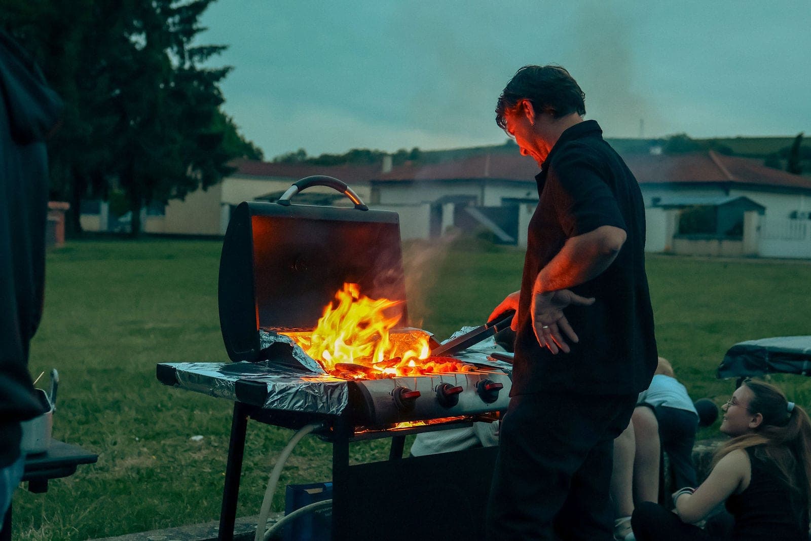 Le barbecue allumé au crépuscule, les flammes hautes.
