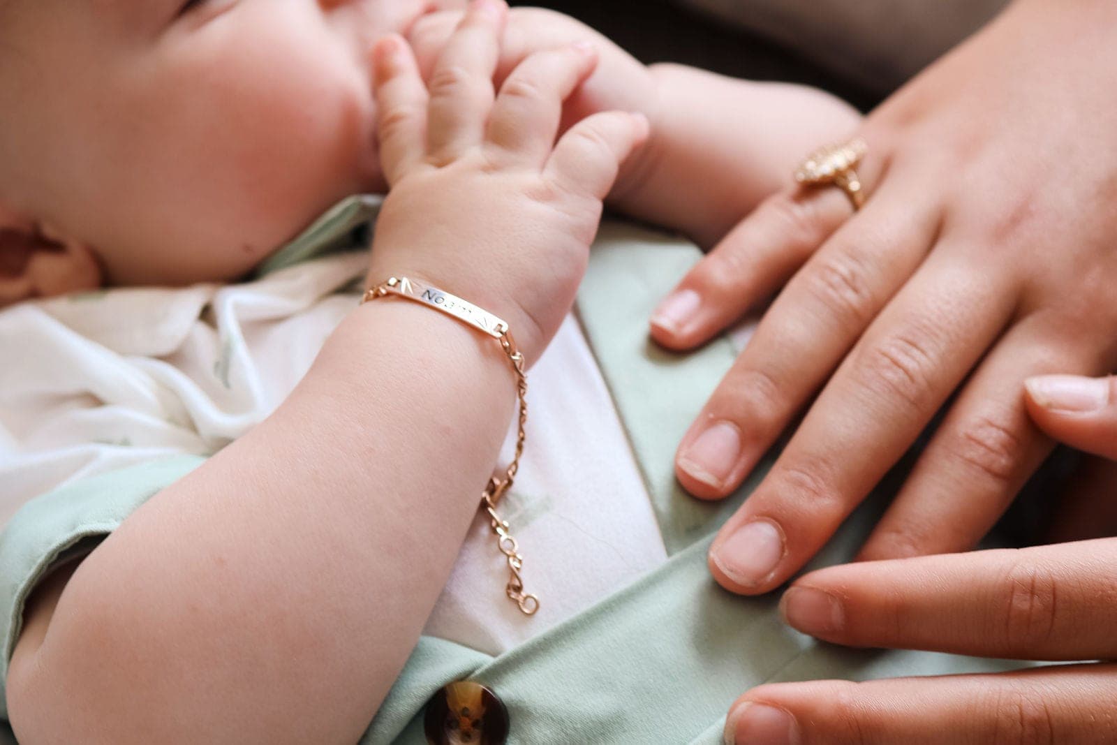 La petite gourmette au poignet, tenue par les mains de sa maman.