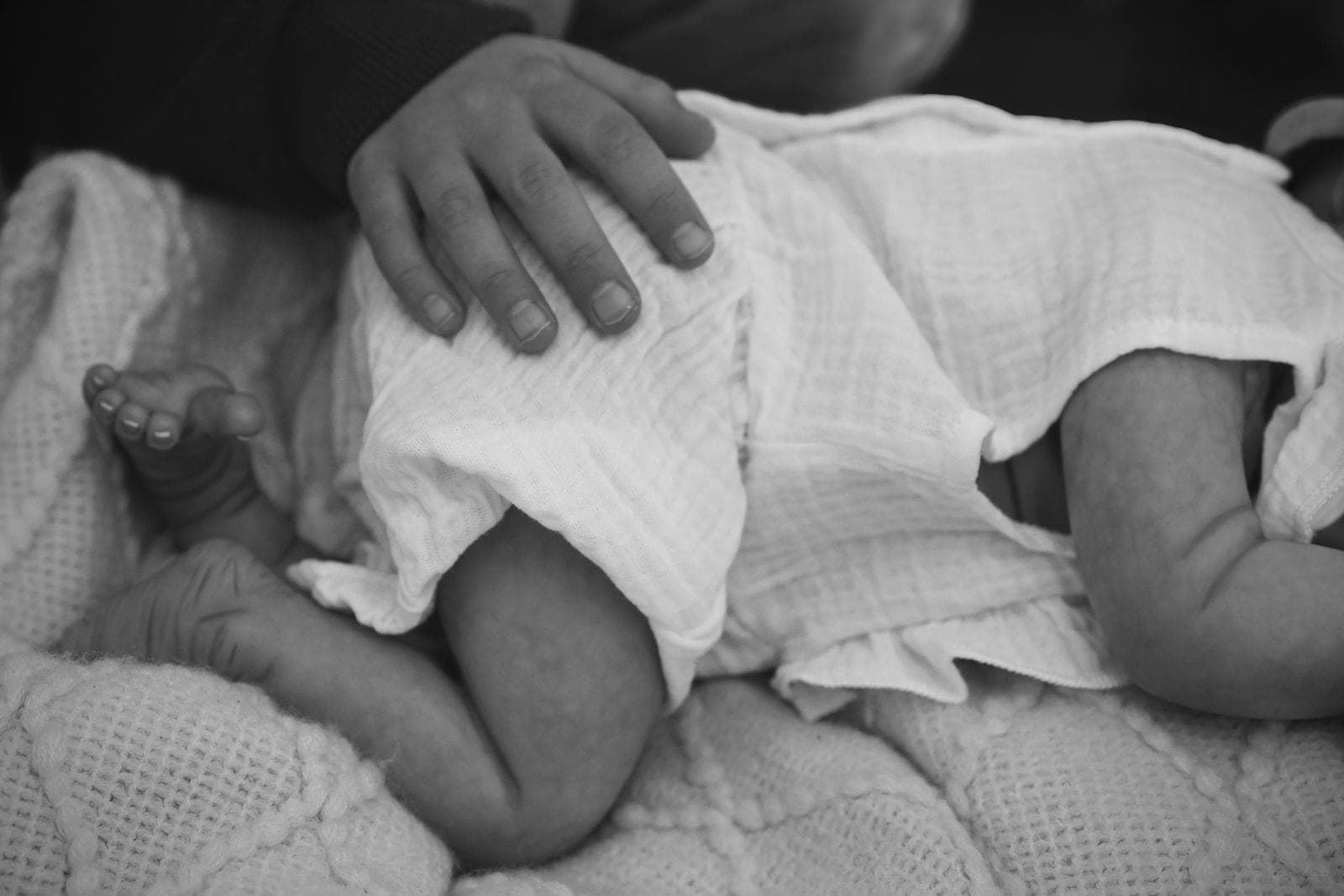 En noir et blanc, la main d’un parent posée sur le lange d’un nouveau-né endormi.