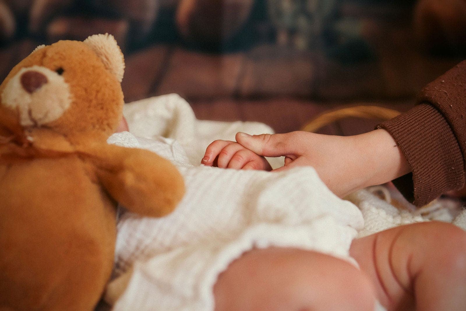 Un ourson veille sur bébé endormi, sa petite main tenue par celle de sa maman.