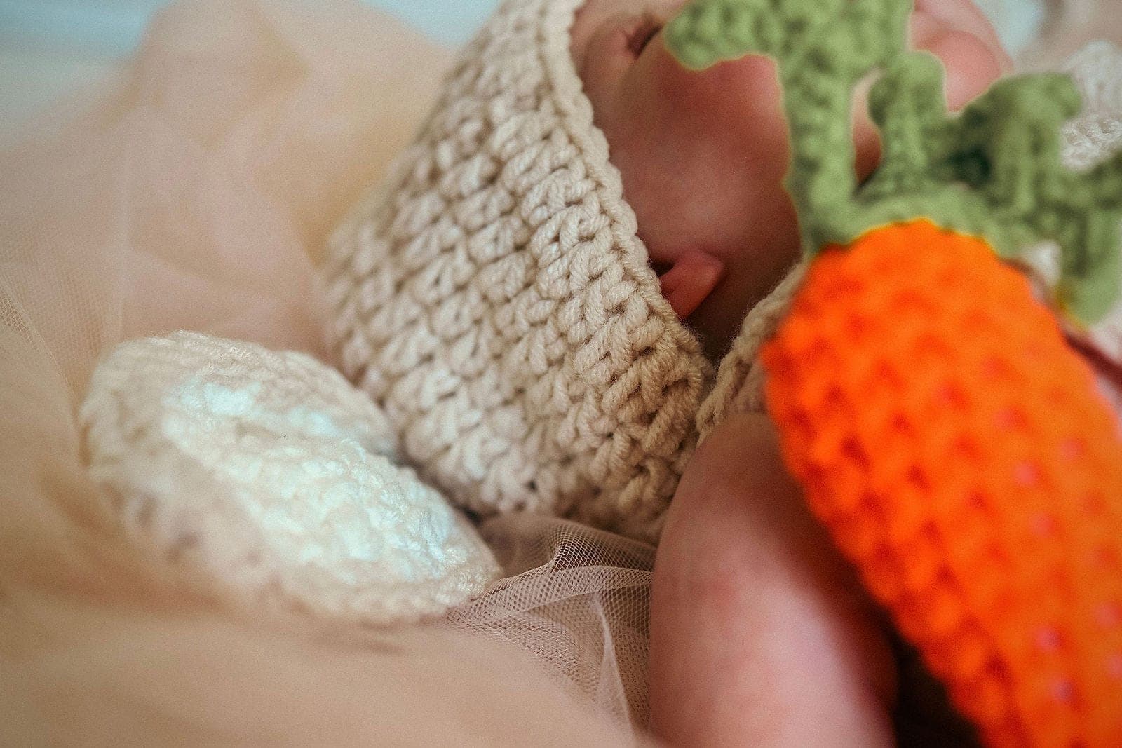 Gros plan sur le bonnet de laine et la carotte au crochet, tout près du visage de bébé.