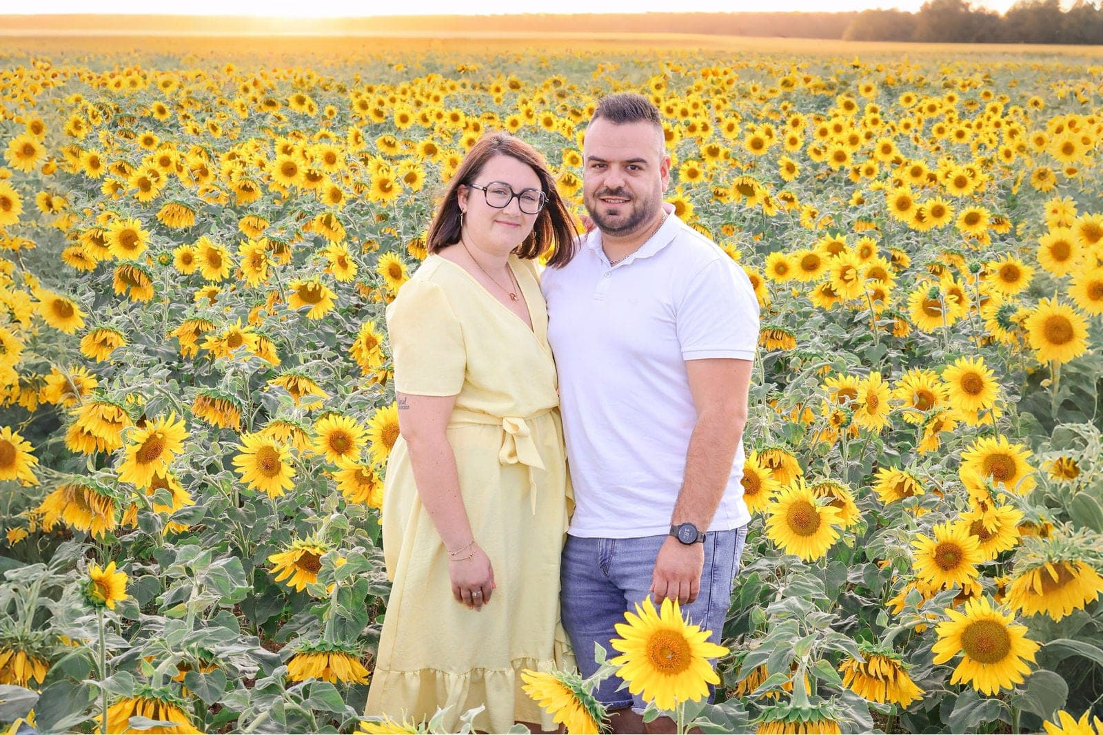 Un couple pose au milieu d’un champ de tournesols en fleurs.