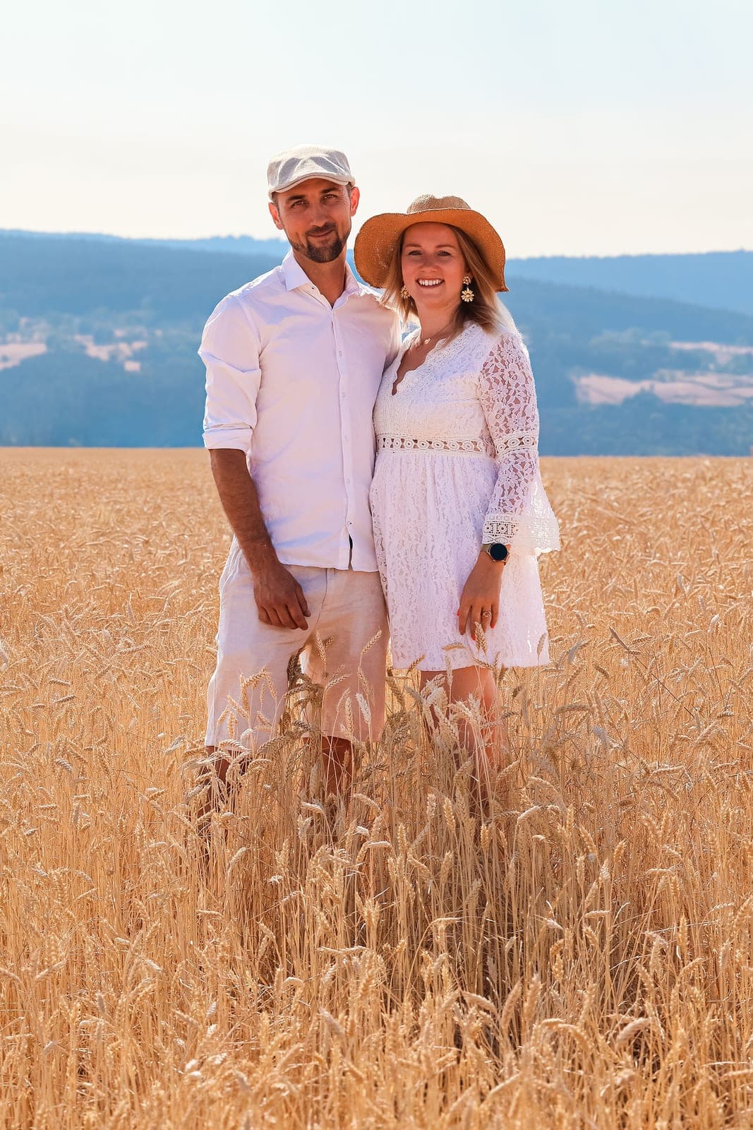 Un couple dans les blés dorés, chapeau de paille et tenues blanches.
