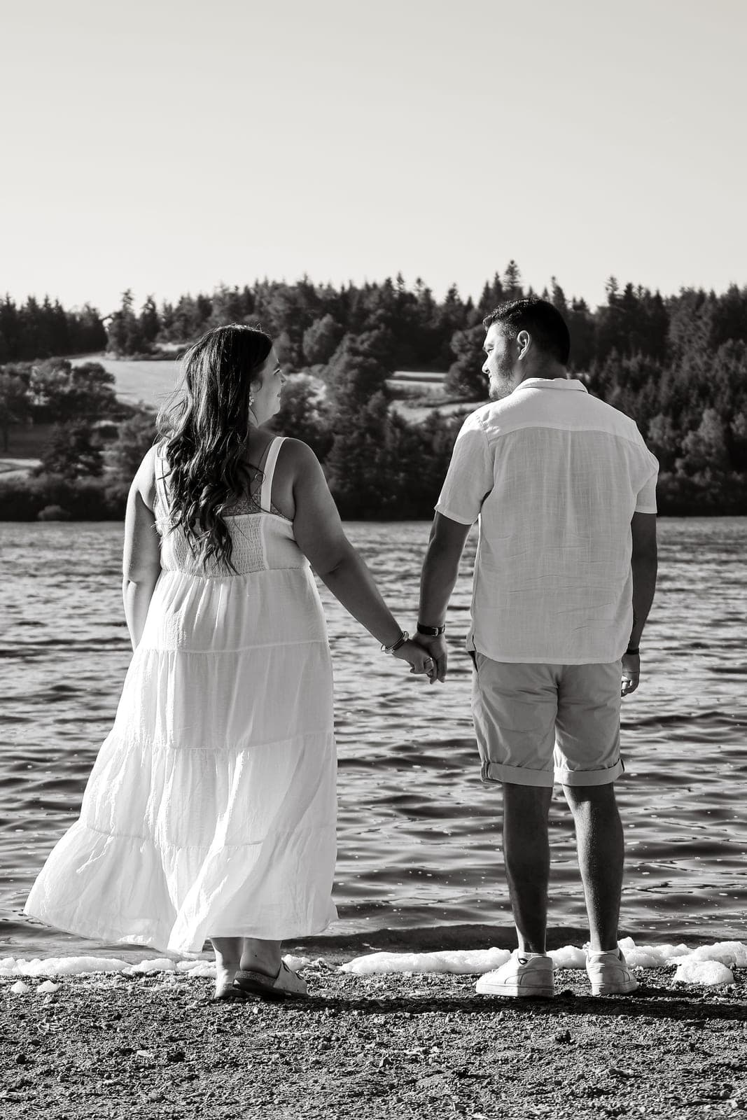 En noir et blanc, le couple marche main dans la main vers le lac.