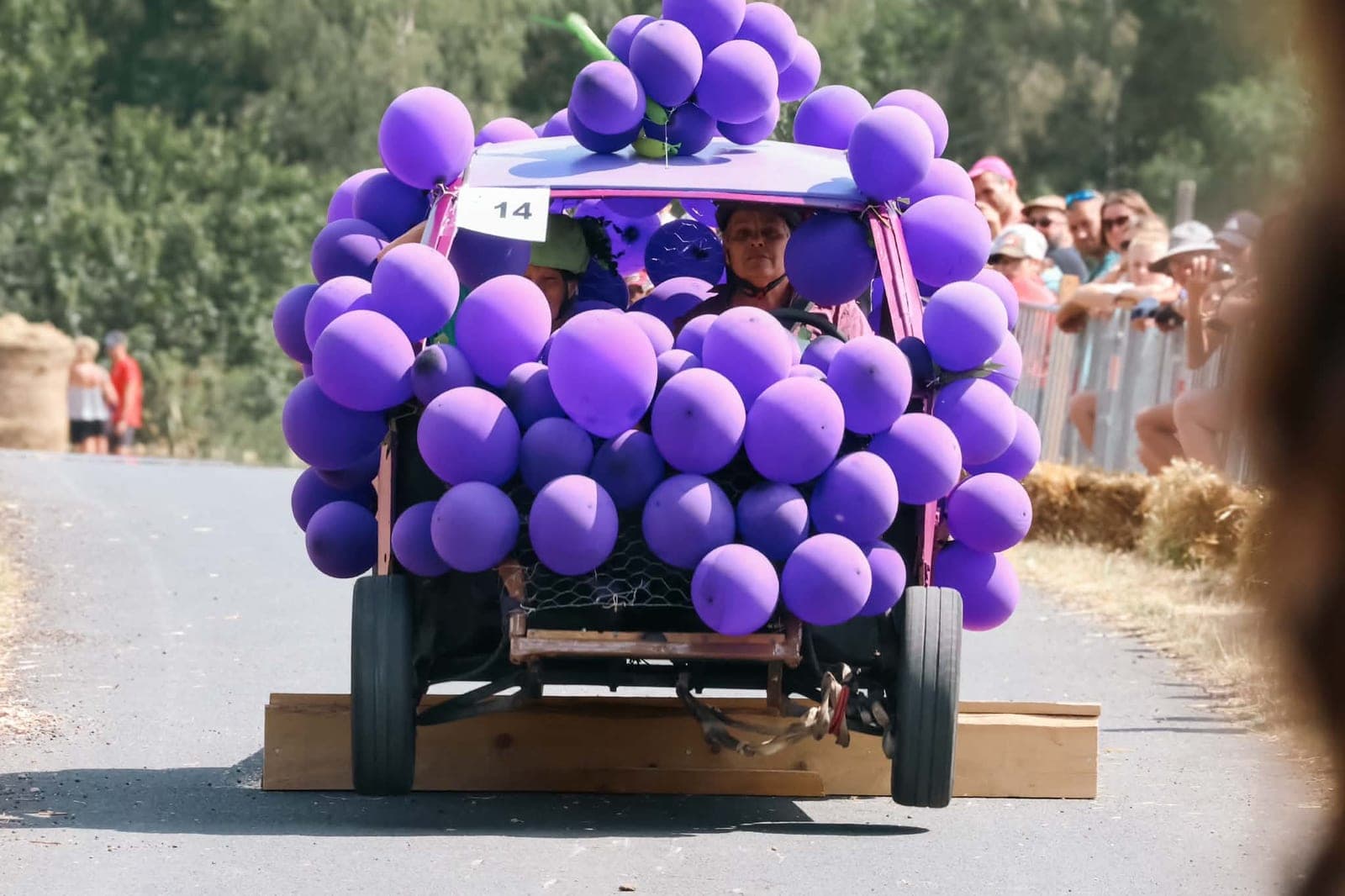 Une caisse à savon habillée en grappe de raisin, couverte de ballons violets, dévale la route devant le public.
