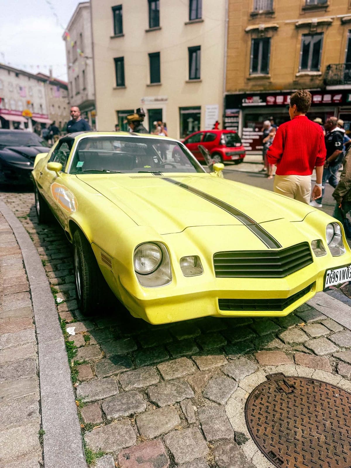 Une Chevrolet Camaro jaune à bande noire, alignée le long du trottoir pavé.