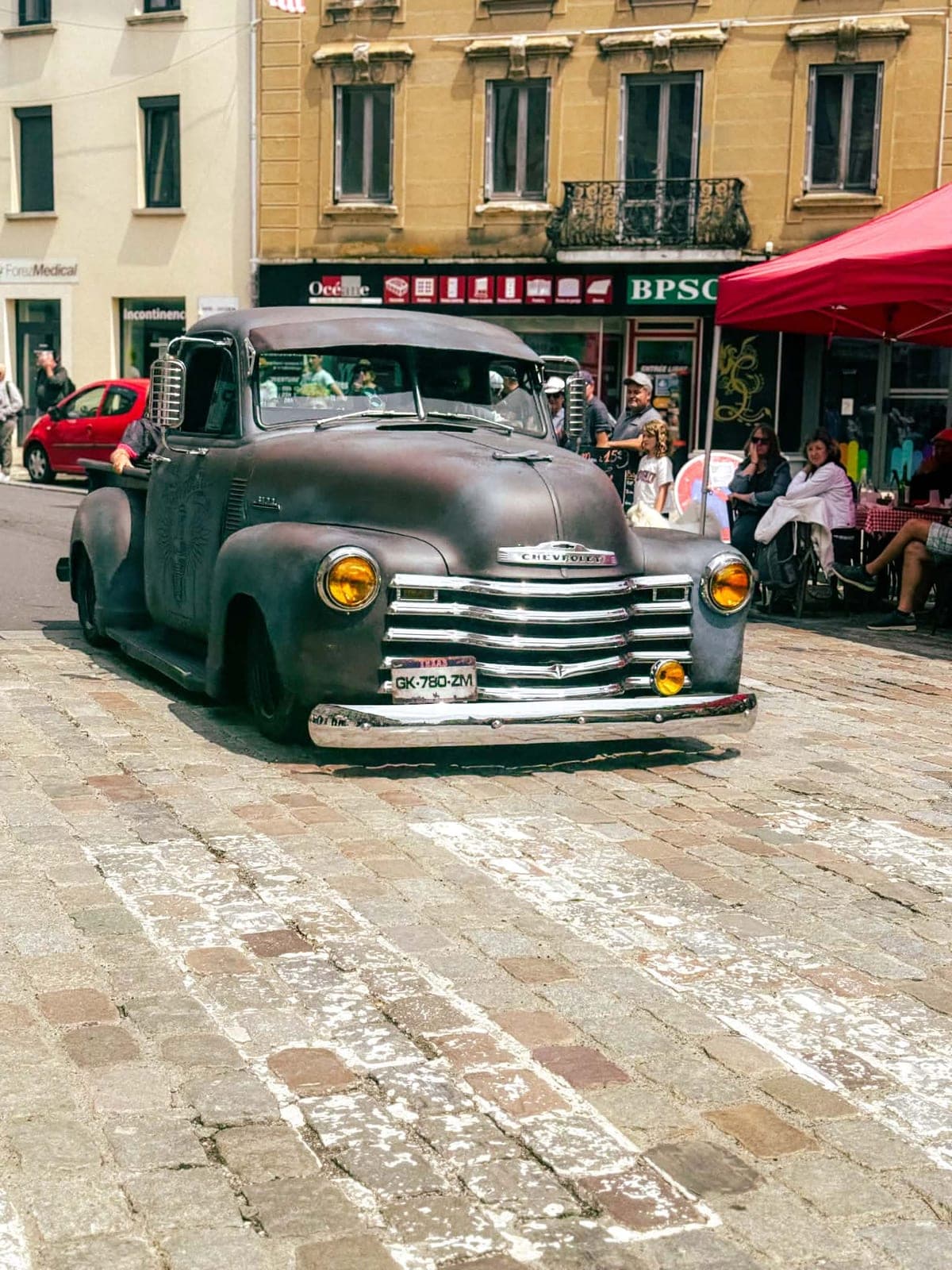 Un pick-up Chevrolet ancien à la carrosserie patinée, chromes au soleil, garé sur la place.