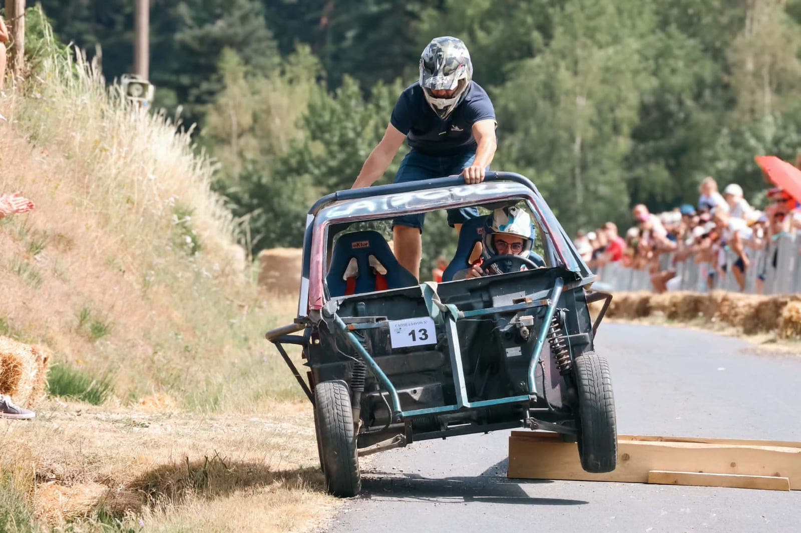 Une caisse à savon décolle du tremplin, roue avant en l’air, un équipier debout à l’arrière.