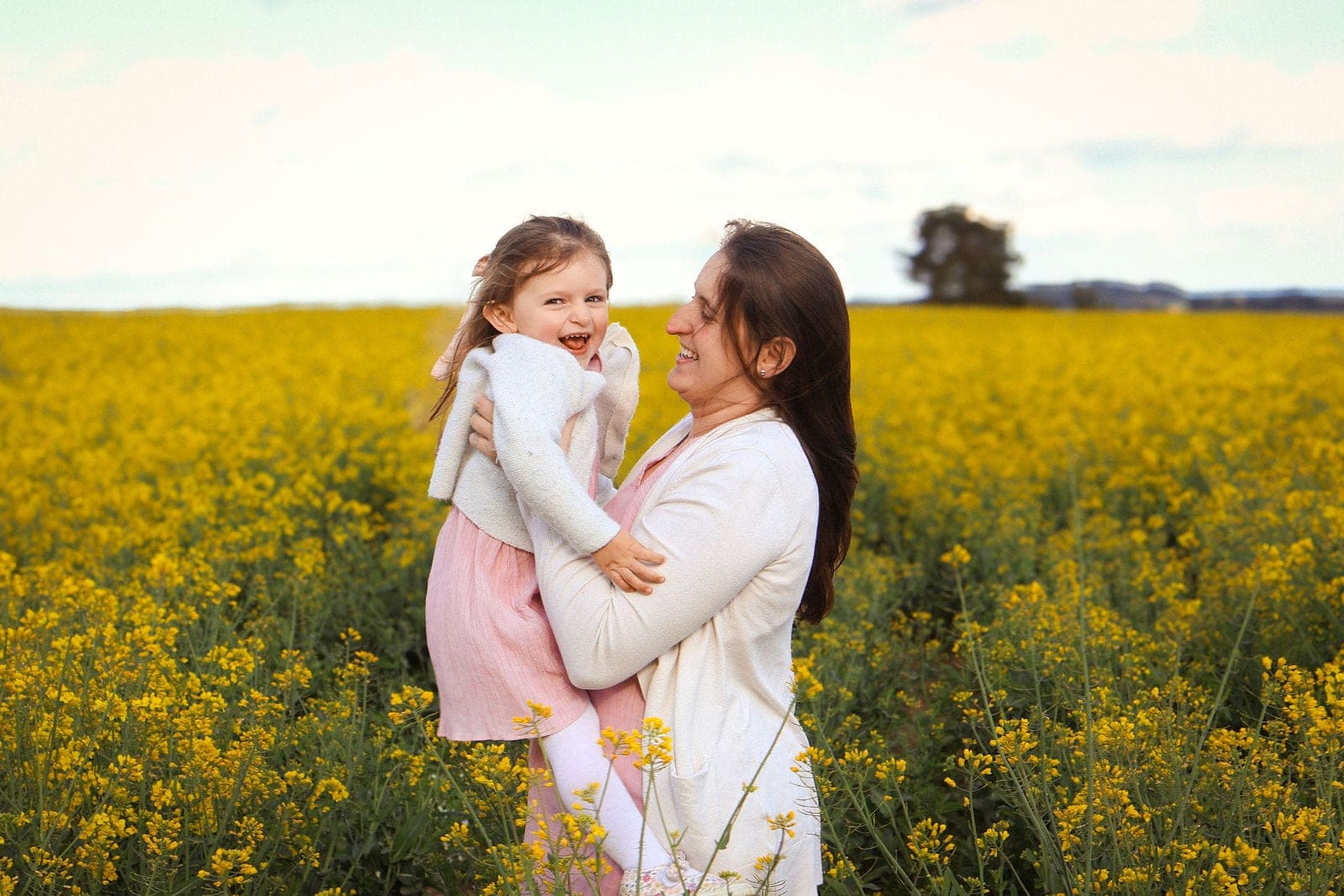 Une maman soulève sa fille dans un champ de colza en fleurs.