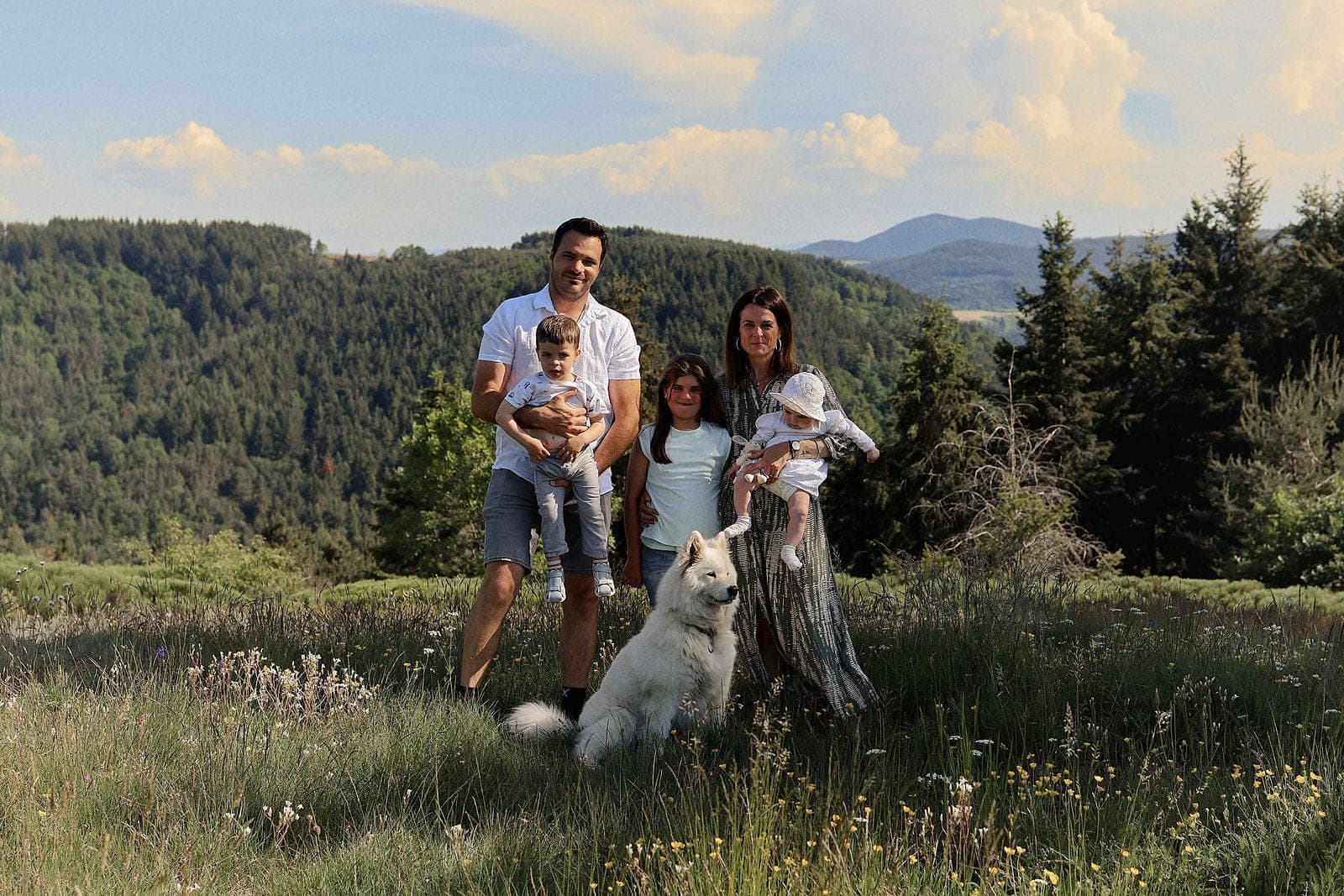 Une famille et son chien blanc assis sur un tronc, au milieu du plateau et de ses forêts.