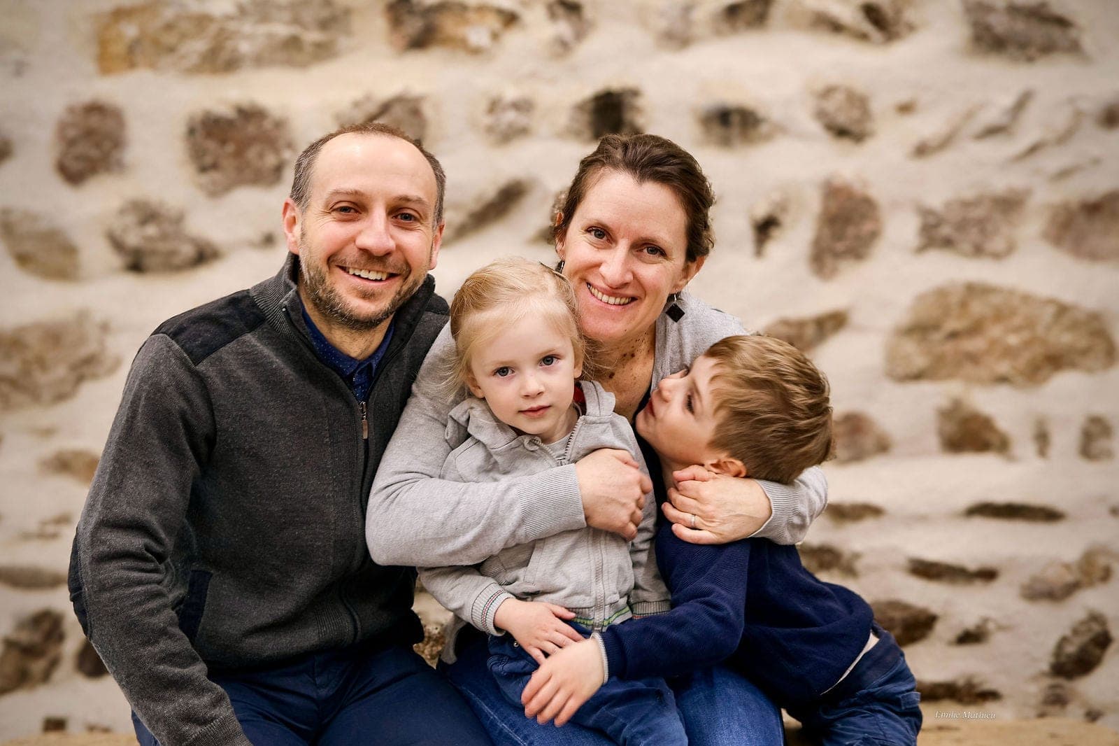 Les parents et leurs trois enfants blottis les uns contre les autres, devant le mur de pierre.