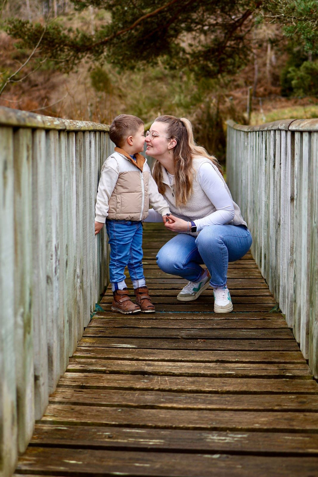 Un bisou sur la passerelle de bois, entre une maman accroupie et son petit garçon.