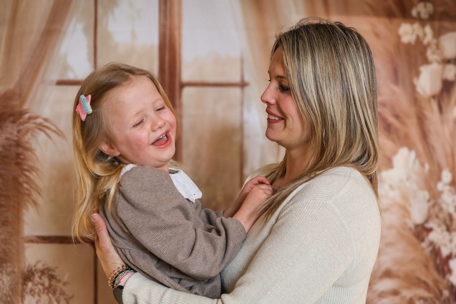 Une petite fille éclate de rire dans les bras de sa maman, au studio.