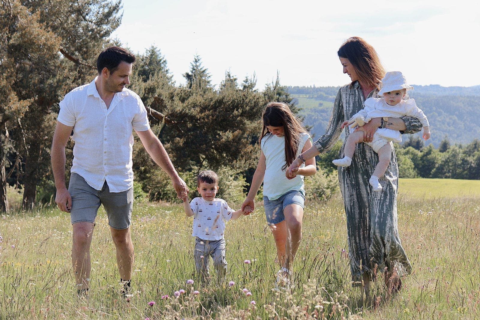 Une famille de cinq marche main dans la main dans les hautes herbes.