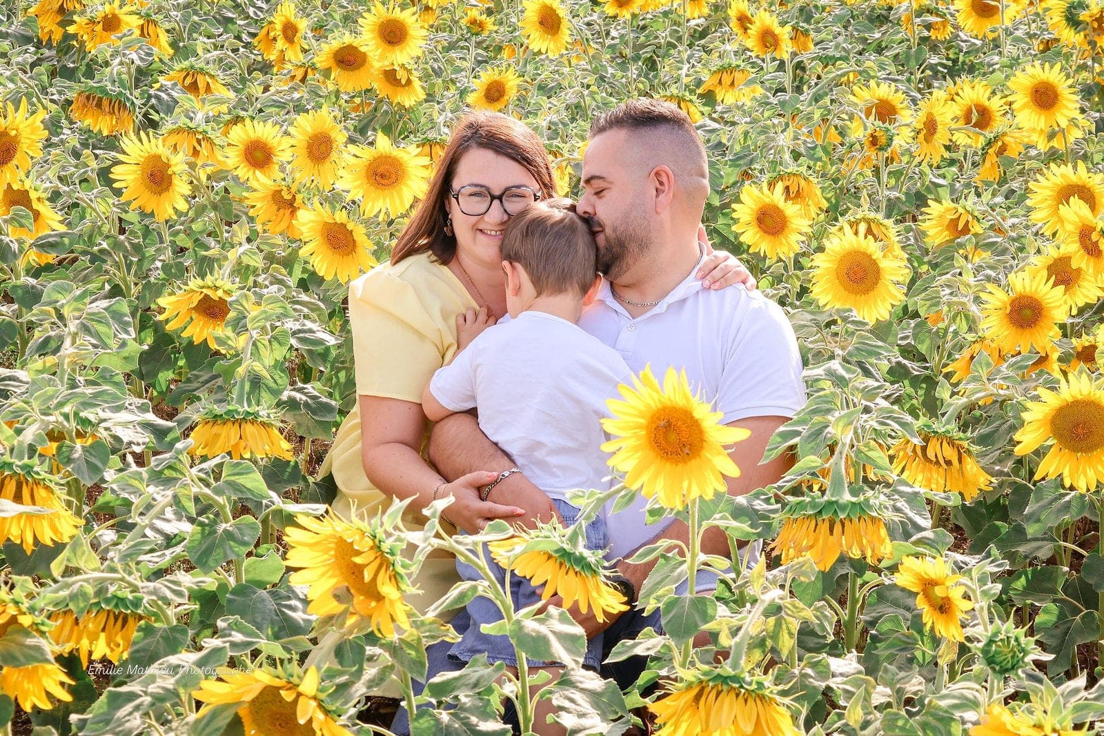 Les parents et leur petit garçon au cœur d’un champ de tournesols en fleurs.
