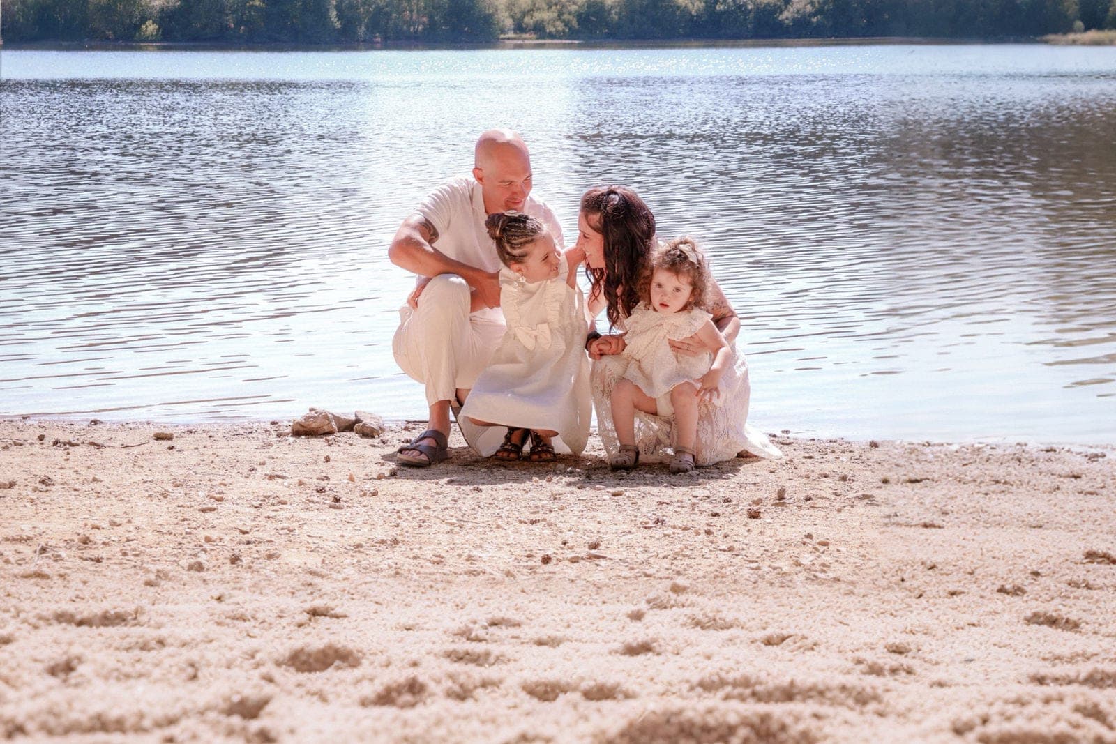 Une famille assise sur le sable du lac, en tenues claires et pieds nus.