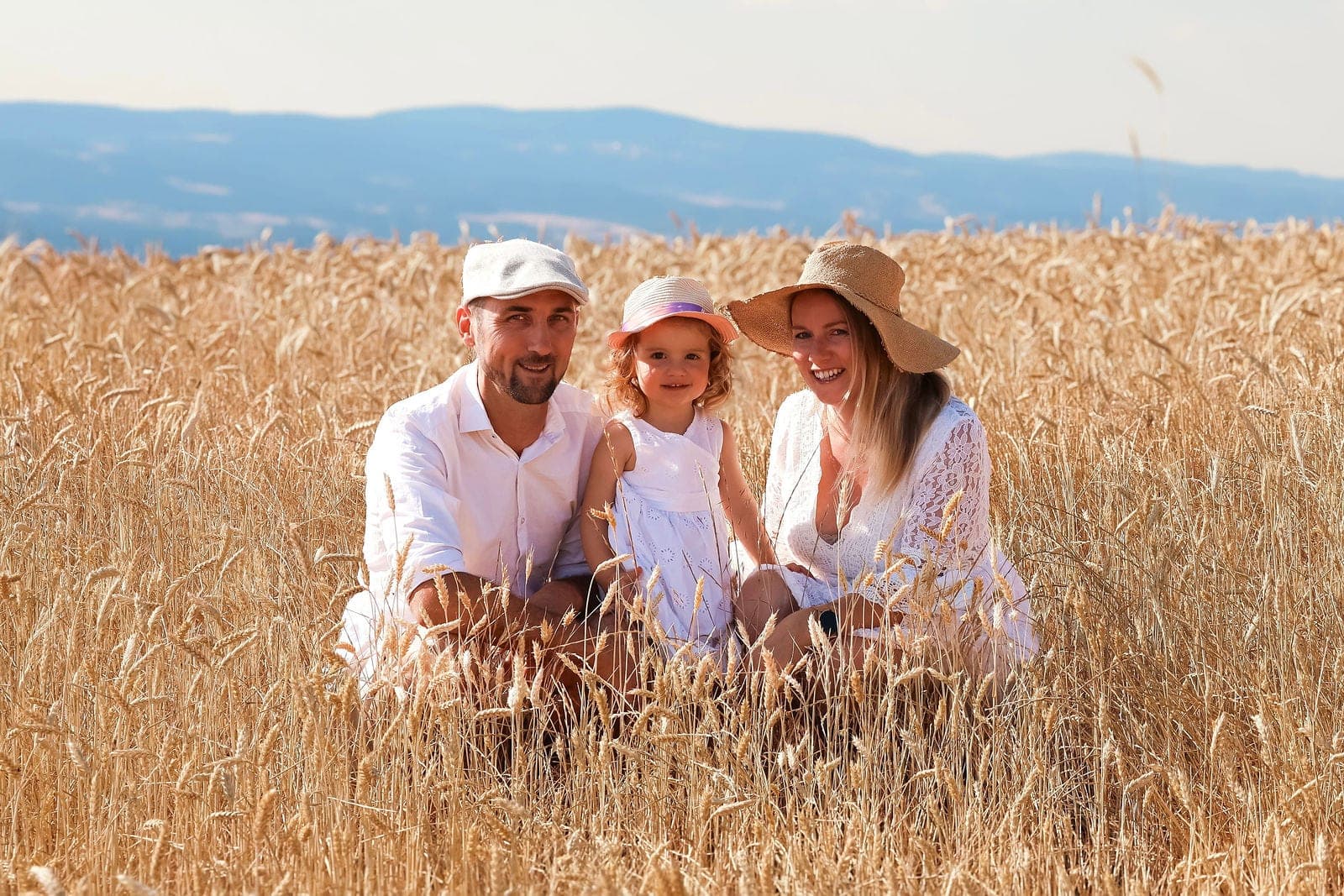 Papa, maman et leur fille assis dans les blés, chapeaux de paille sur la tête.