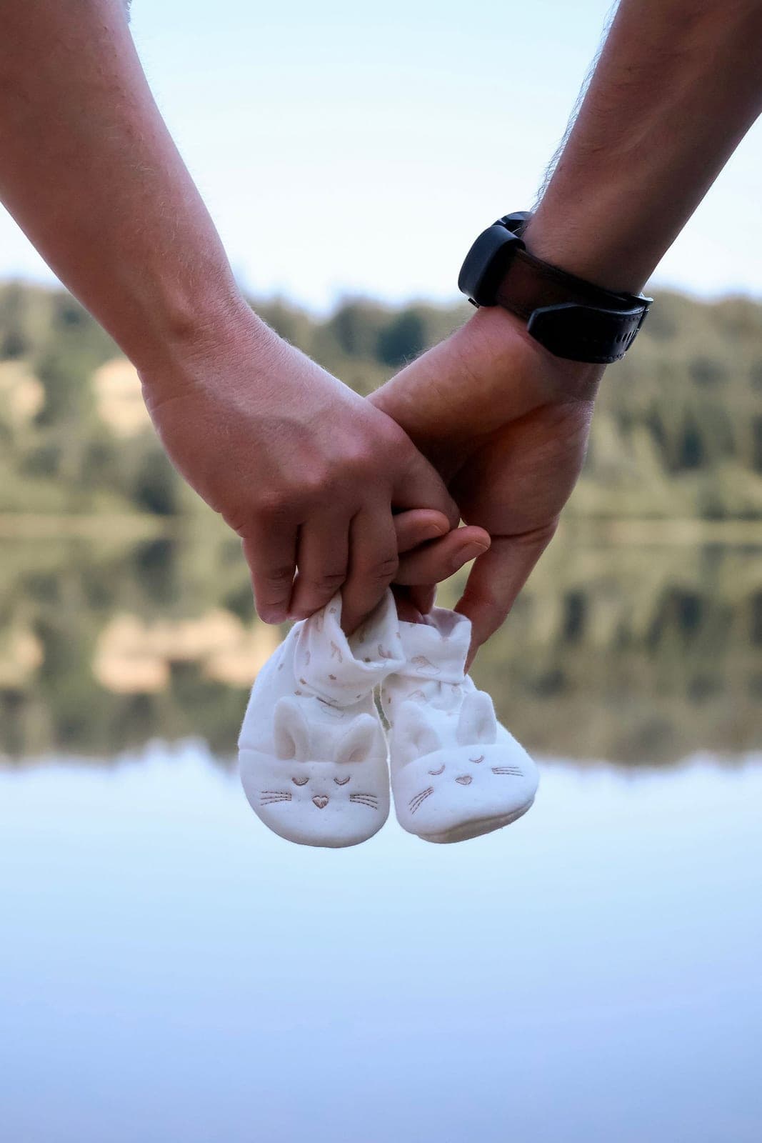 Deux mains tiennent une paire de petits chaussons au-dessus de l’eau.
