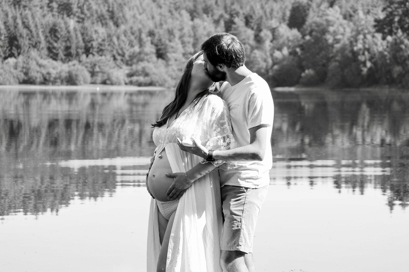 Un couple attend son bébé au bord du lac, en noir et blanc.