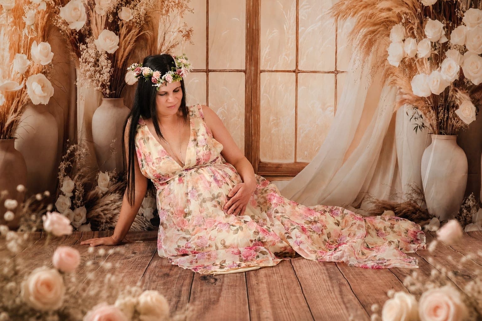 Future maman assise en robe fleurie, couronne de fleurs dans les cheveux.